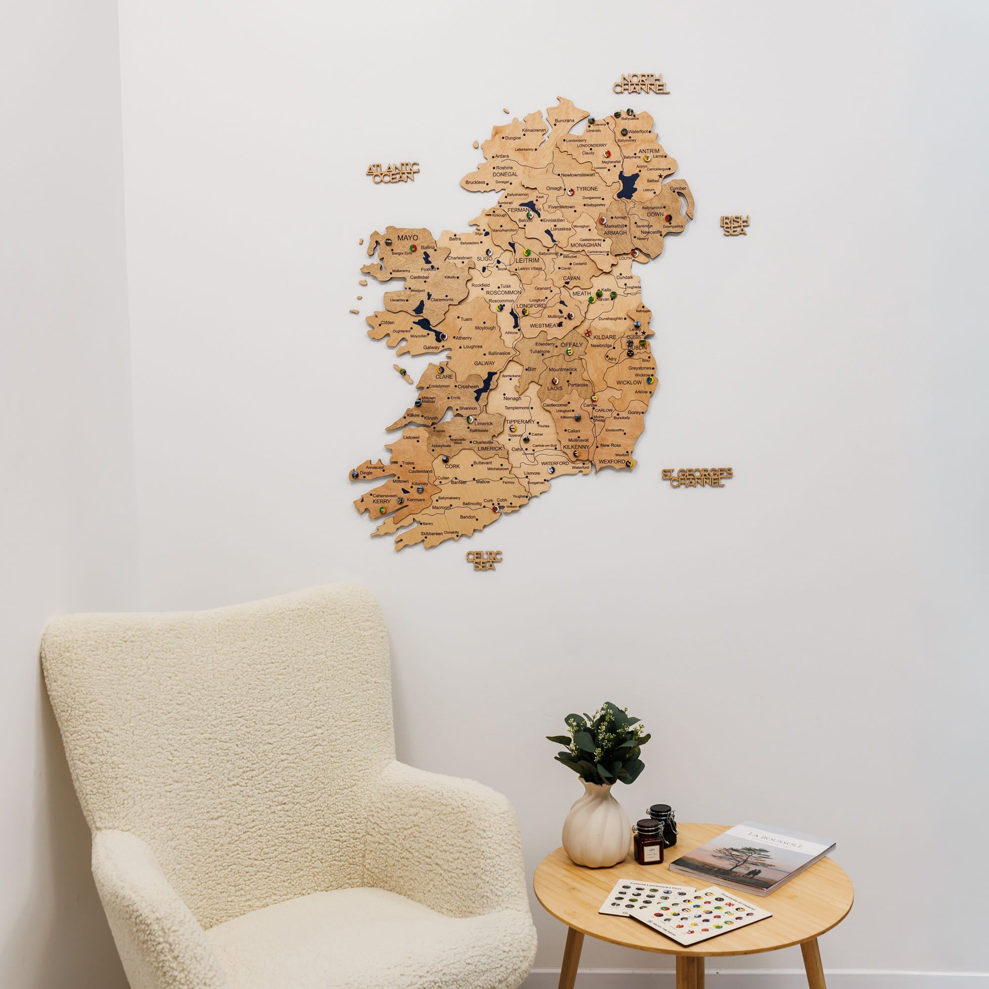 Wooden map of Ireland on a white wall above a beige armchair and small round table.