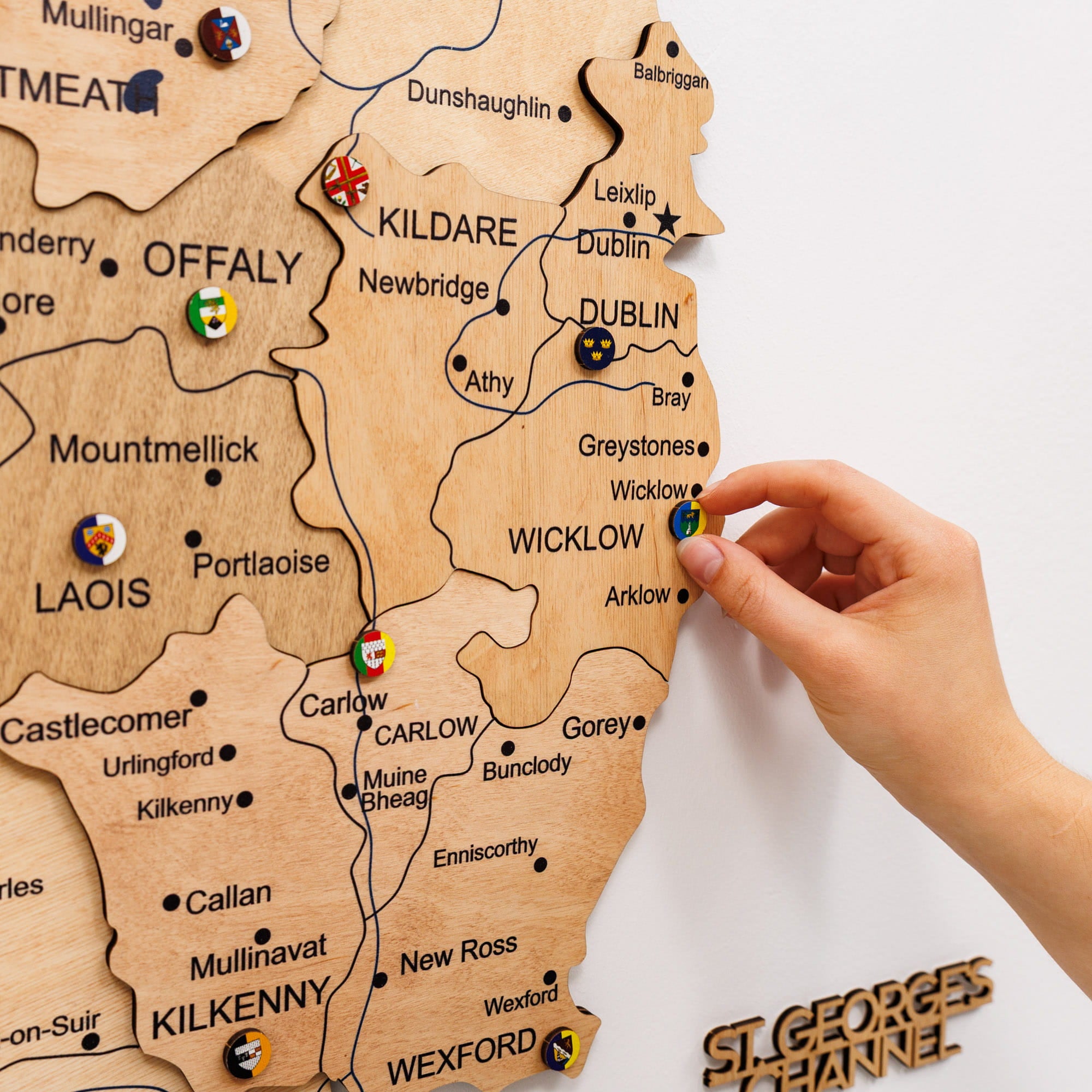 Wooden map of Ireland with pins marking locations, held by a hand.