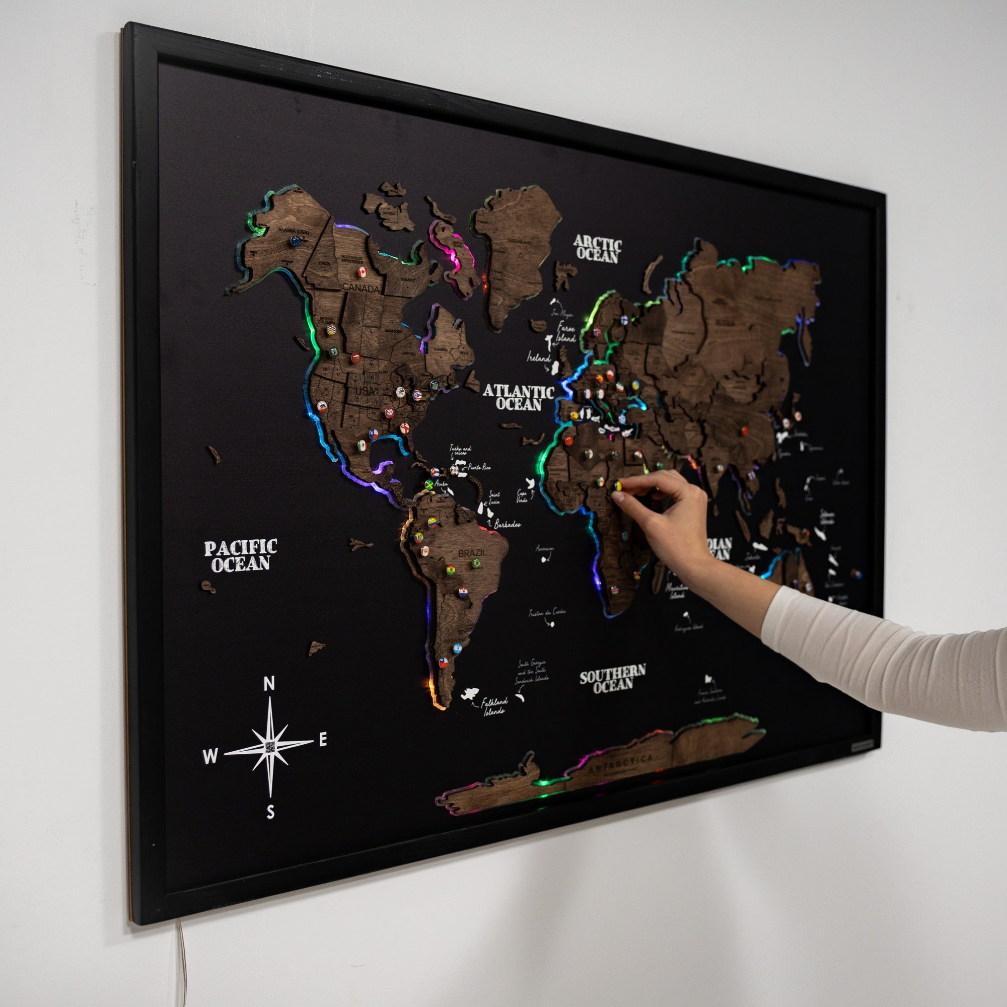 World map with LED lights on a black frame, being touched by a hand.