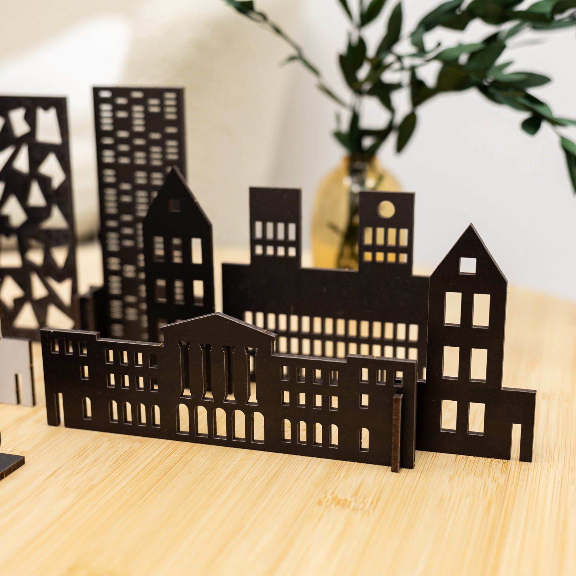 Black cut-out cityscape model on a wooden surface with a plant in the background