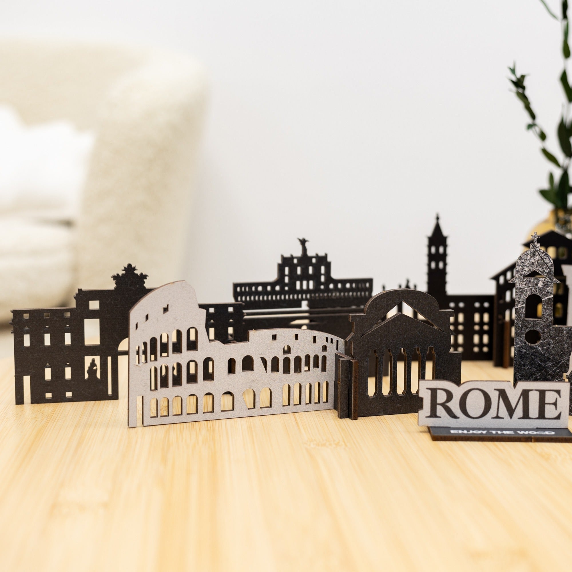 Black cut-out cityscape model of Rome on a wooden surface with 'ROME' sign.
