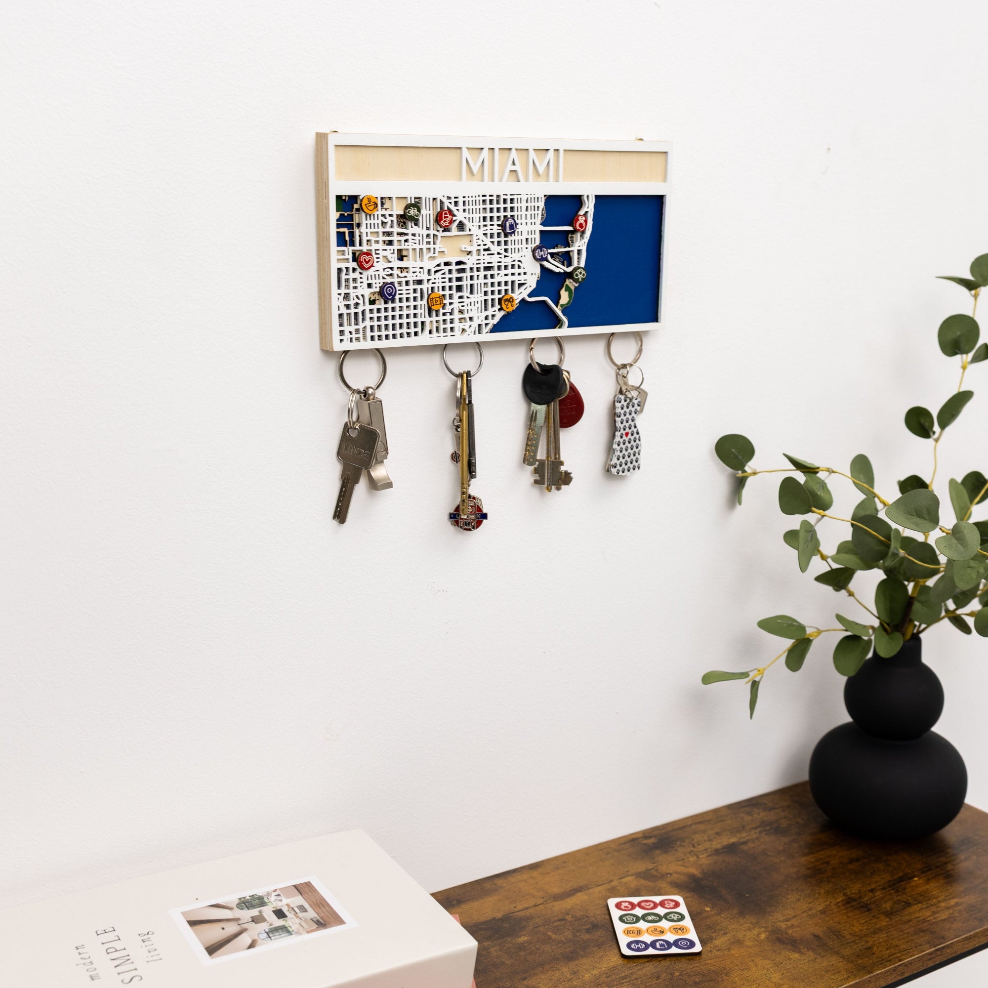 Key holder with keys attached on a wall next to a plant and wooden surface.