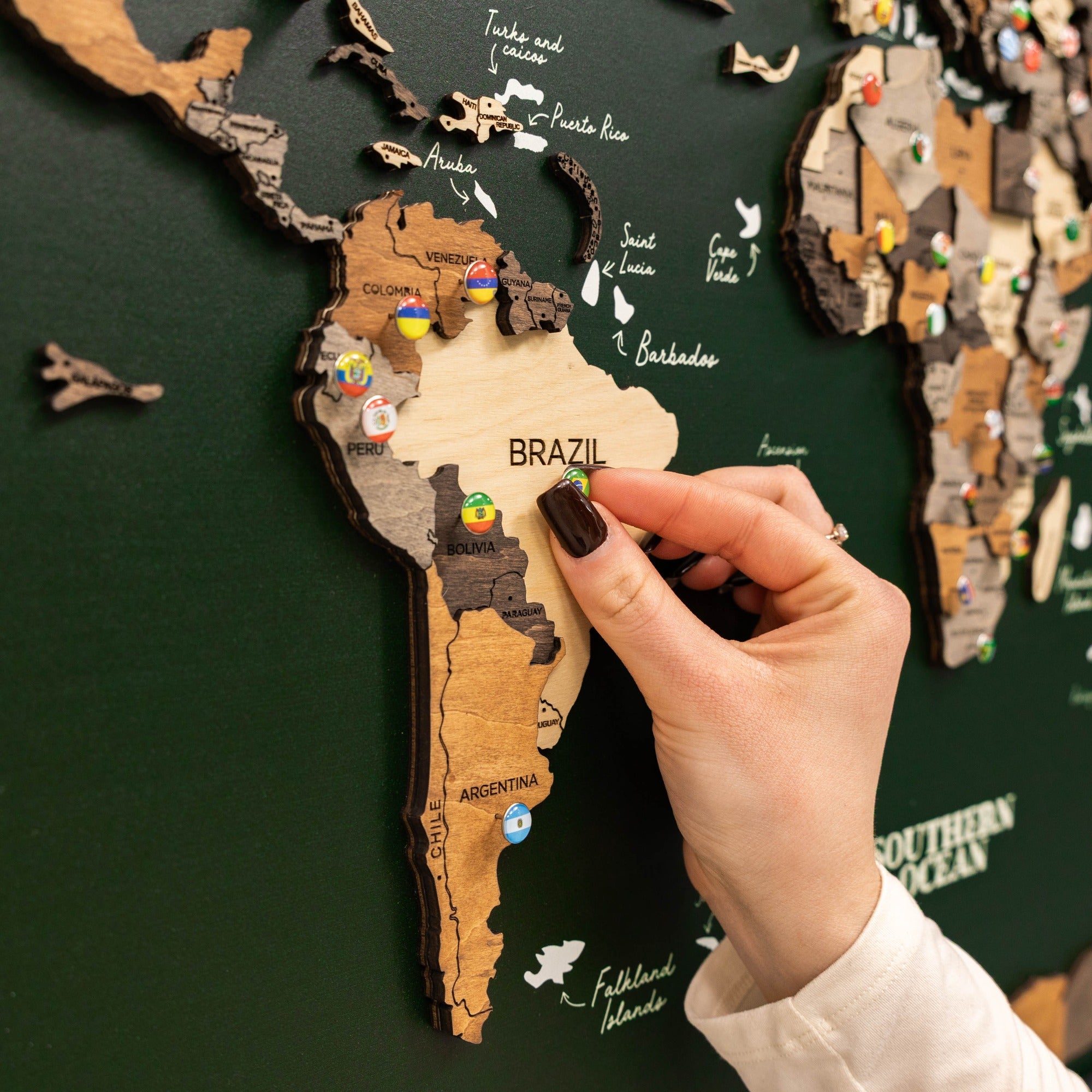 Hand placing a wooden puzzle piece on a map of South America, with 'Brazil' highlighted.