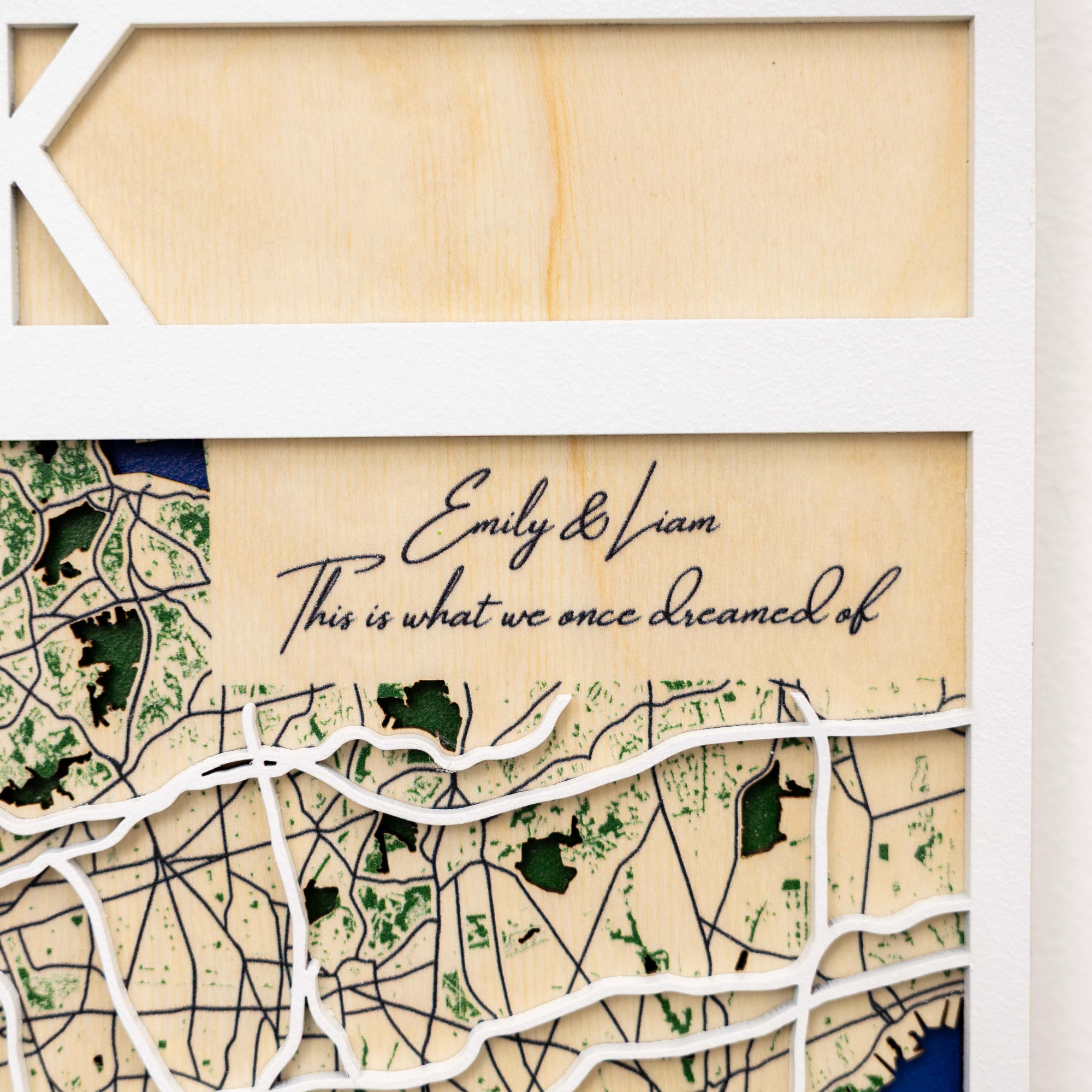 Wooden map with engraved text 'Emily & Liam, This is what we once dreamed of' on a beige background.