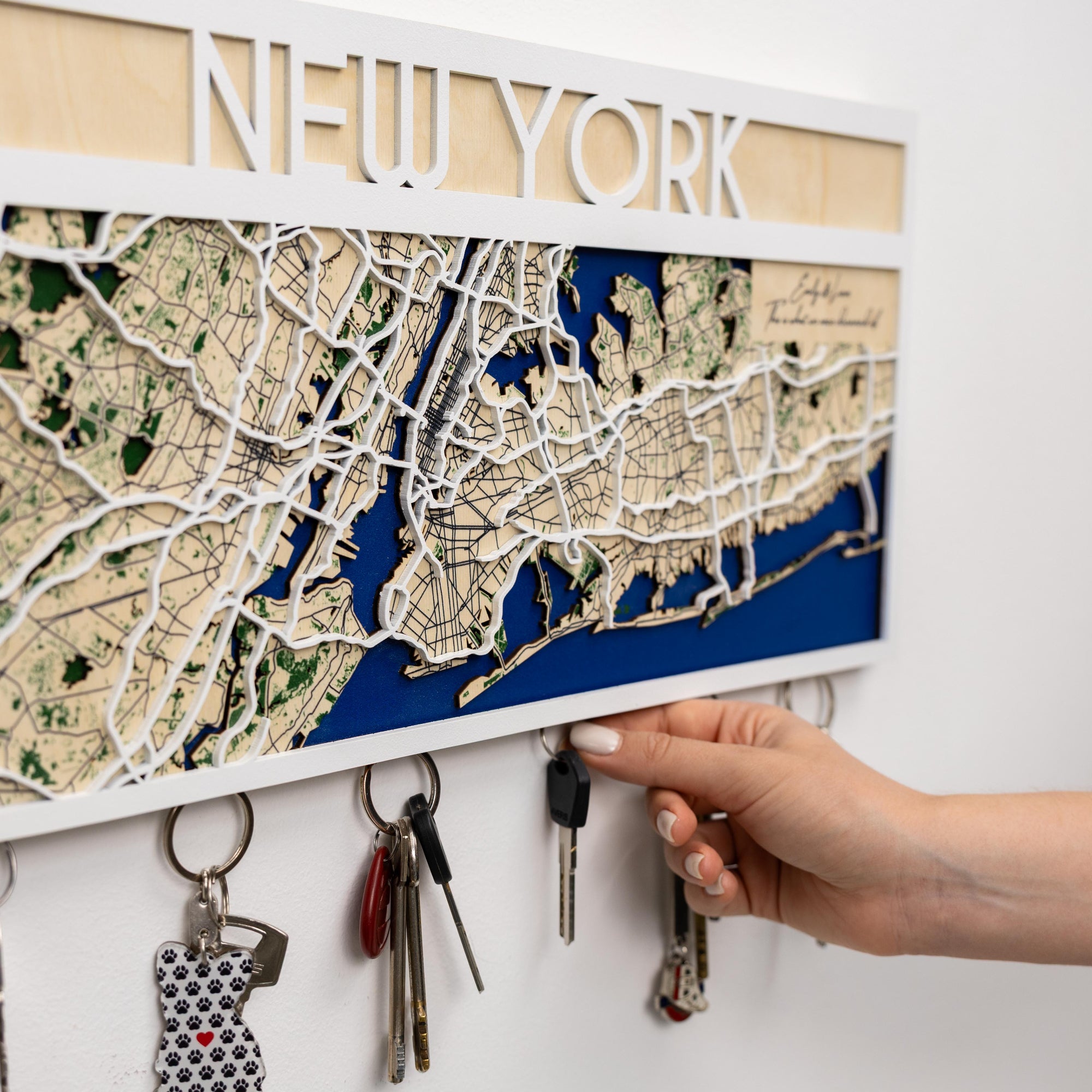 Wooden key holder with New York map design on a white wall.