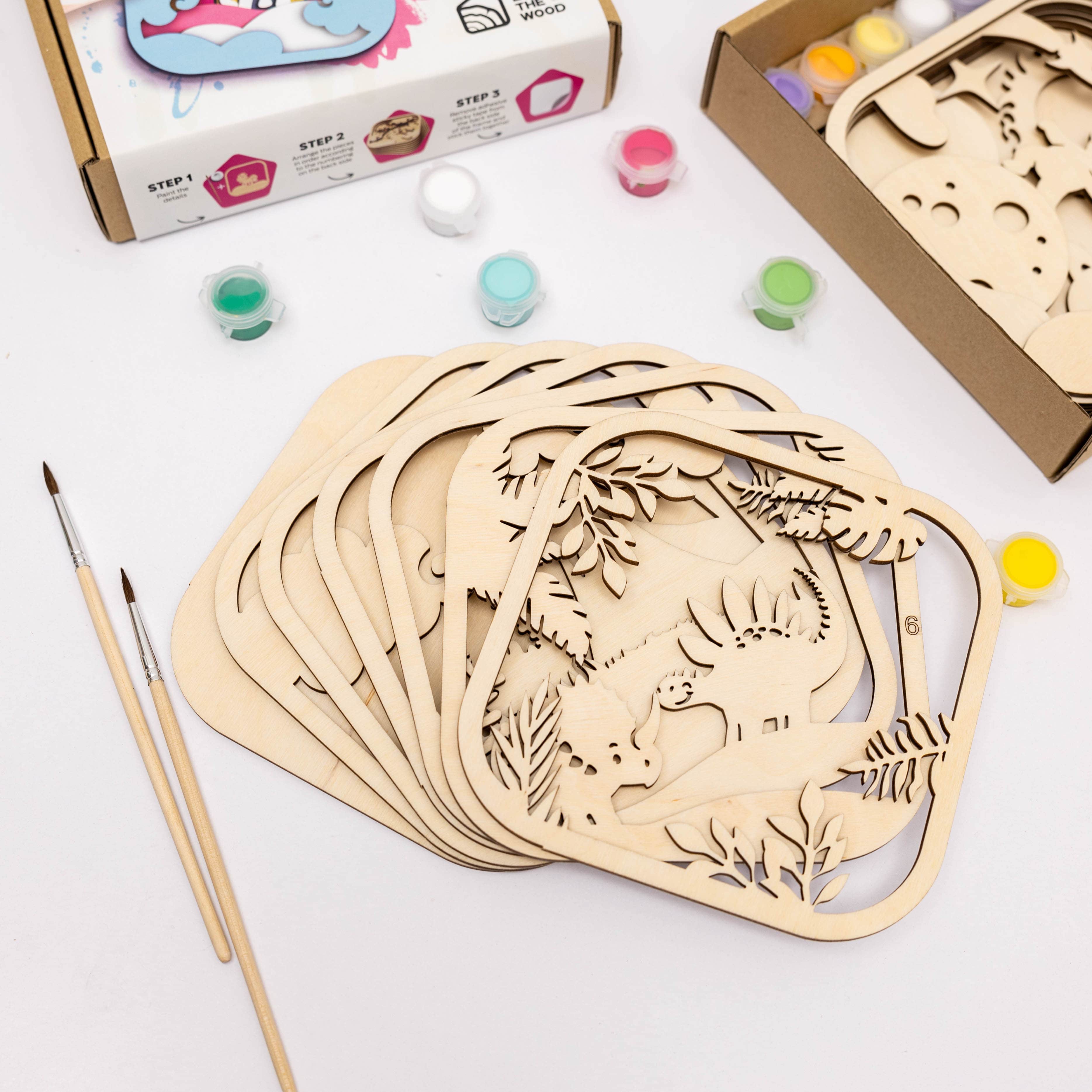 Wooden cut-out shapes with animal designs on a white surface with paint and brushes.