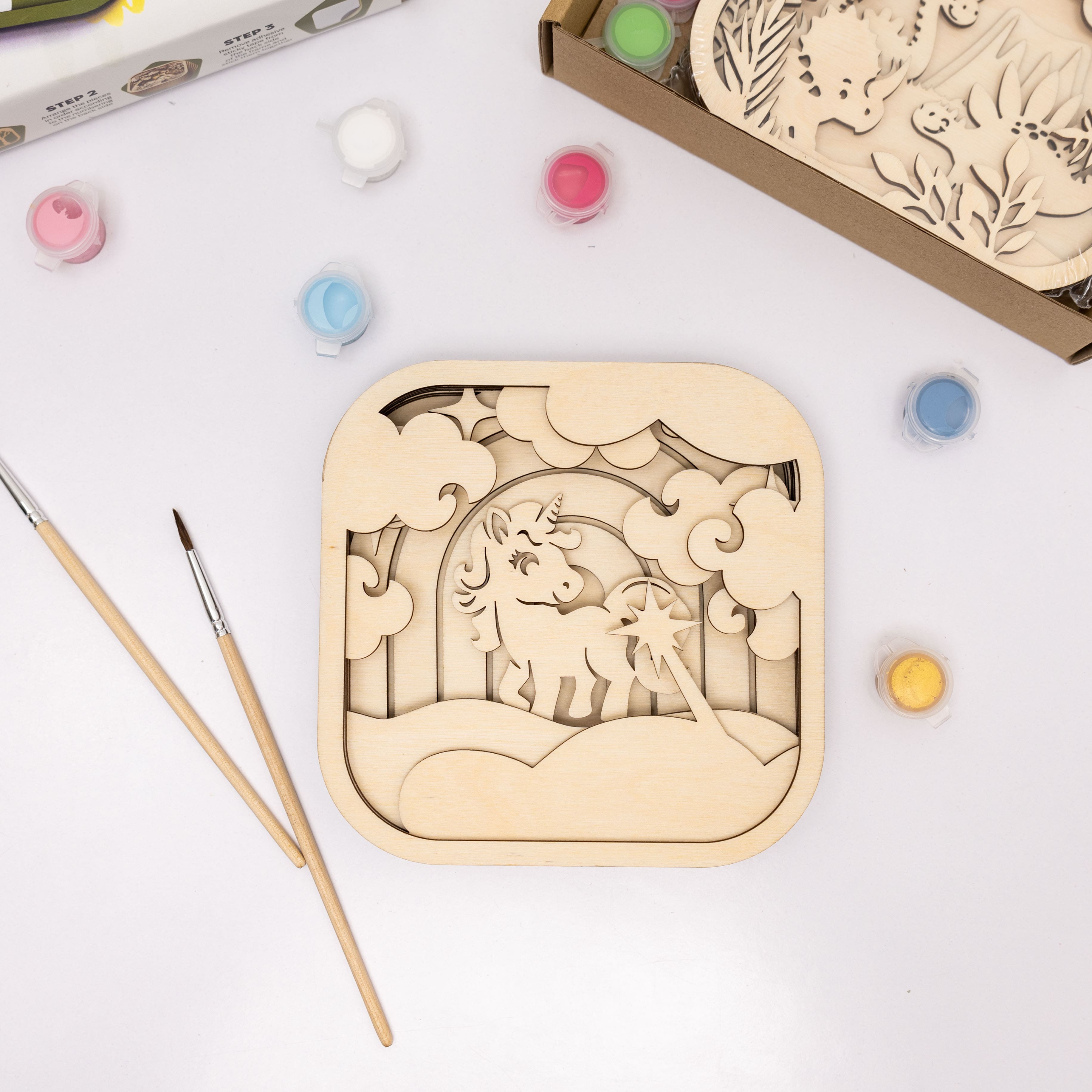 Wooden craft kit with unicorn design, paintbrushes, and colors on a white background