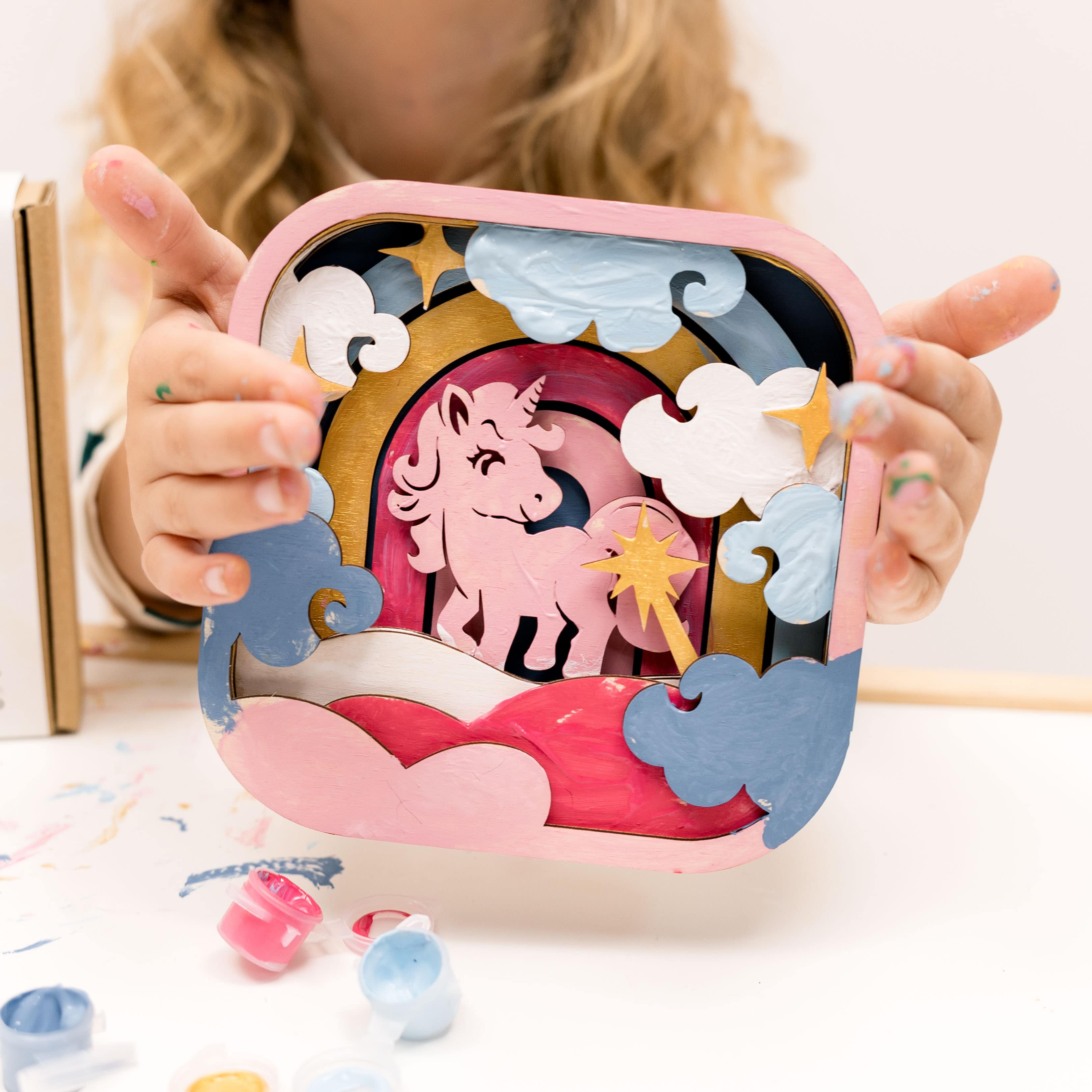 Child holding a unicorn-themed puzzle with colorful pieces on a white surface.