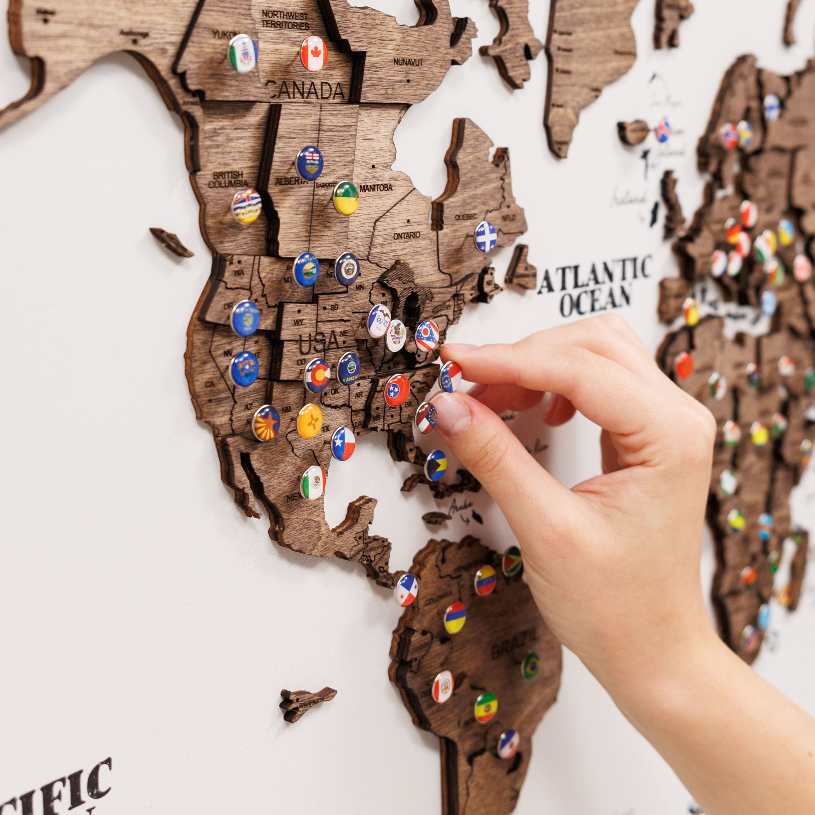 Wooden map of the United States with colorful pins, hand interacting with it.