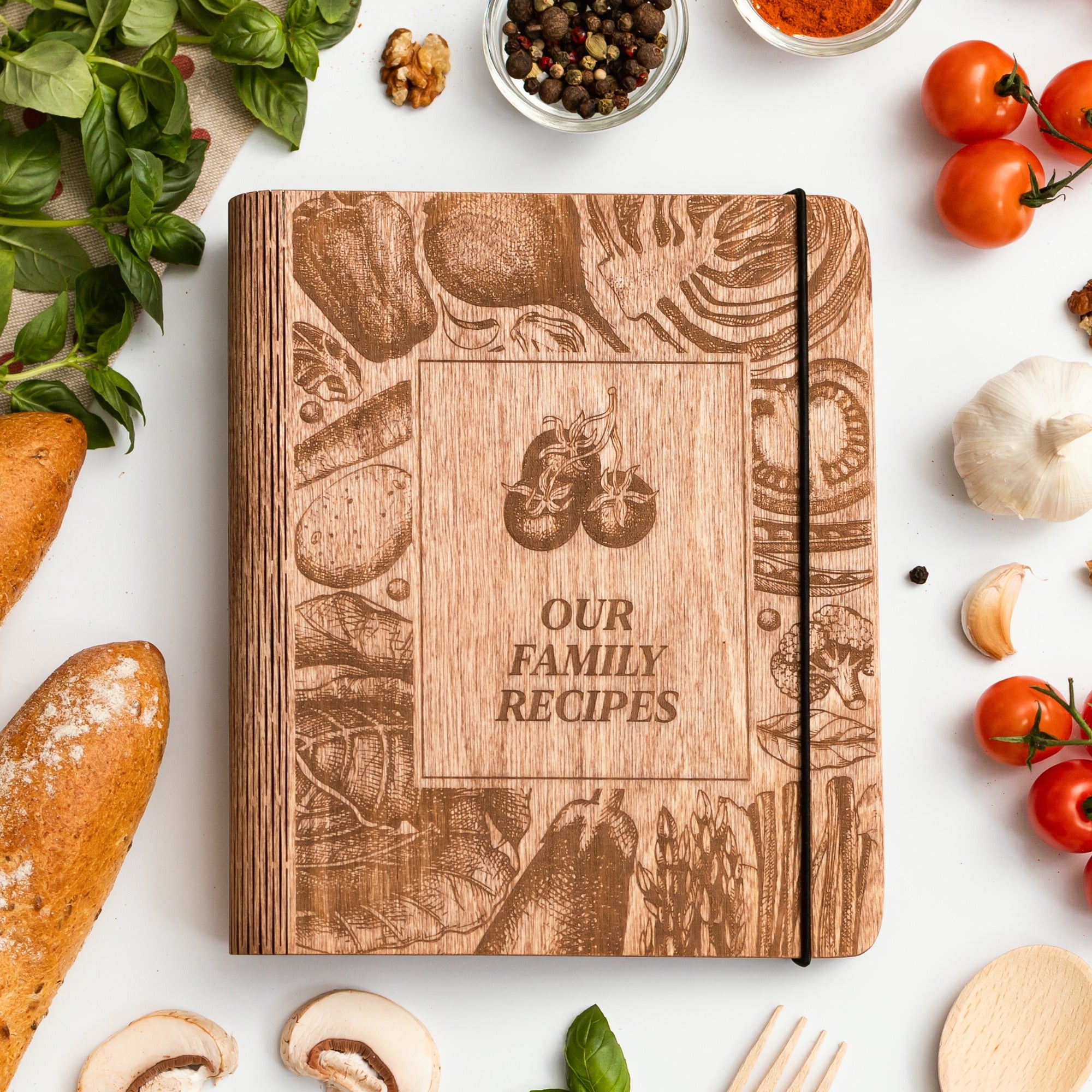 Wooden recipe book titled 'Our Family Recipes' surrounded by kitchen items on a white background