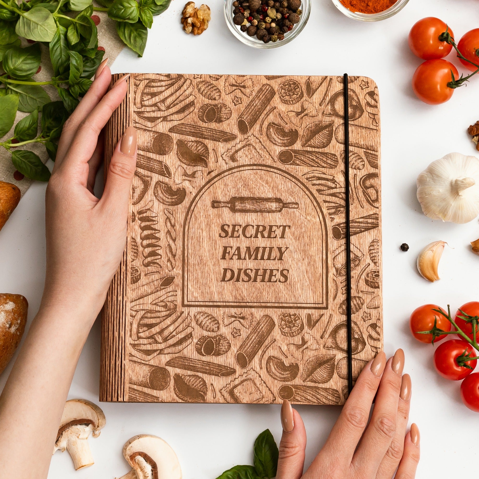 Wooden notebook titled 'Secret Family Dishes' surrounded by kitchen items on a white surface