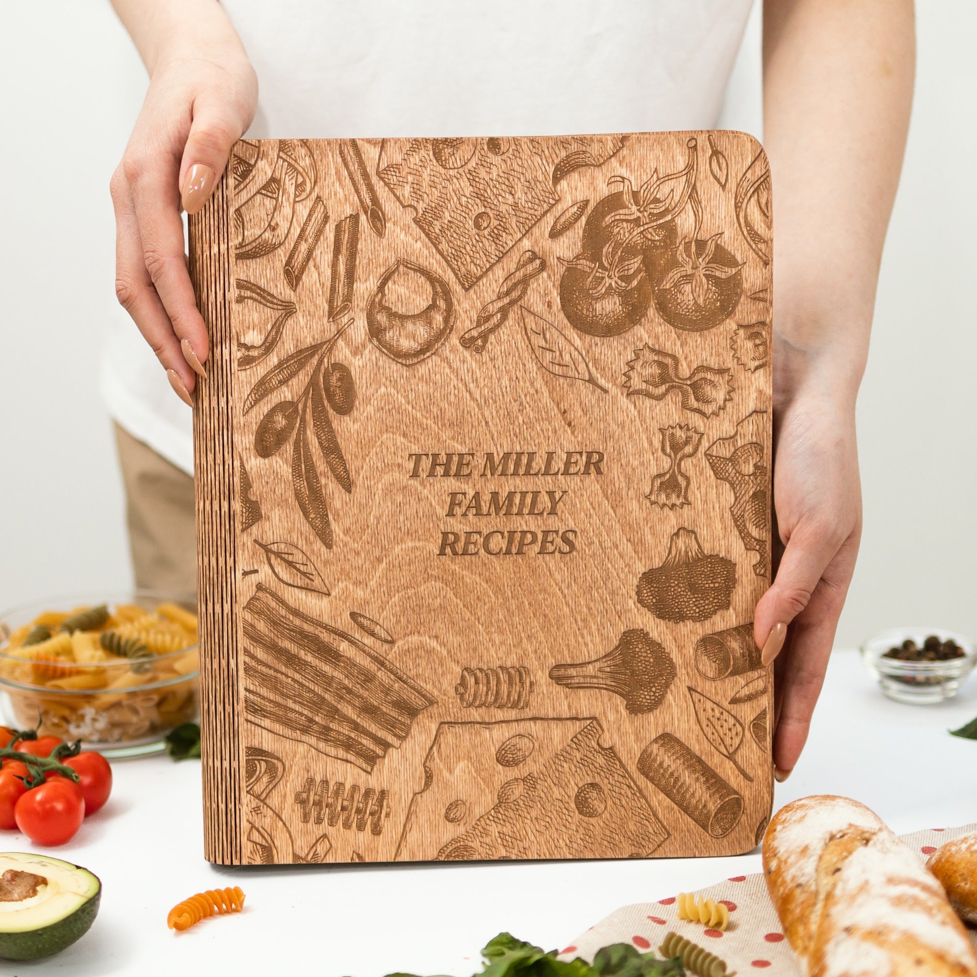 Wooden cookbook titled 'The Miller Family Recipes' held by a person with food items in the background.