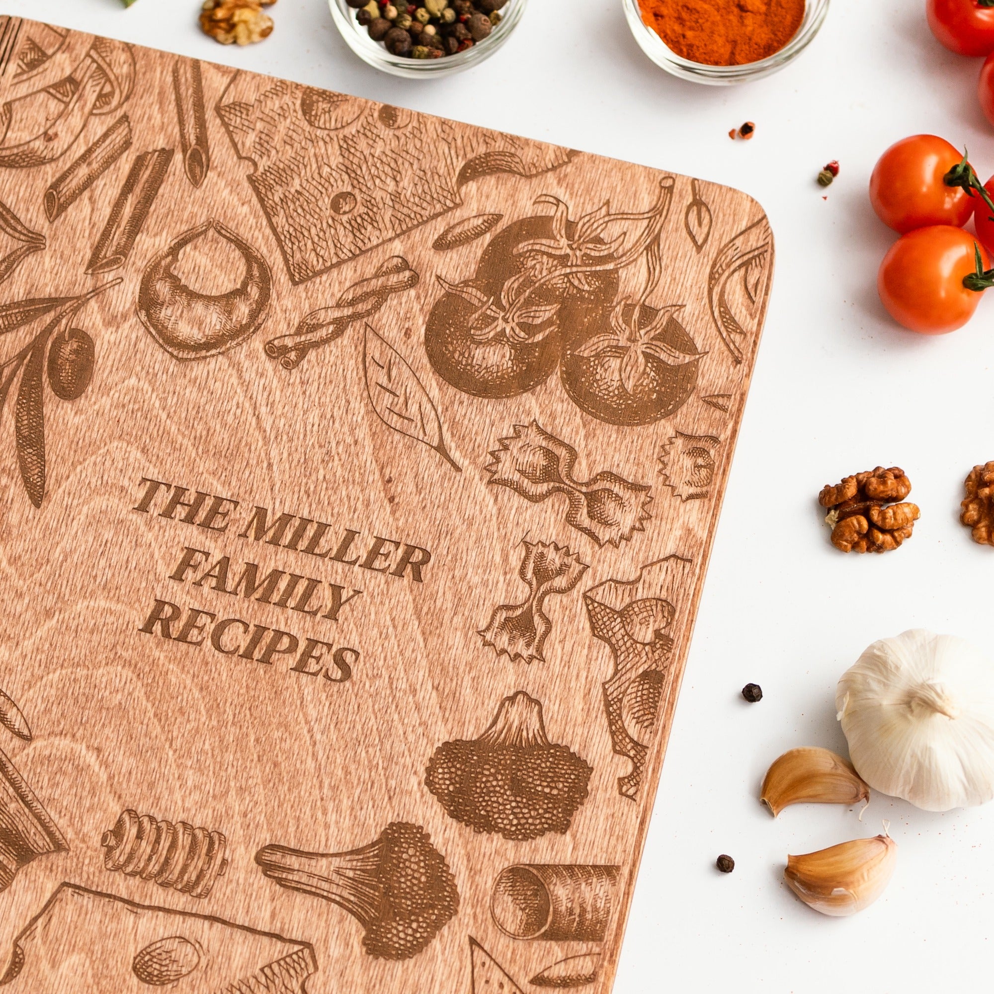 Wooden cutting board with engraved food illustrations and 'The Miller Family Recipes' text, surrounded by kitchen ingredients.