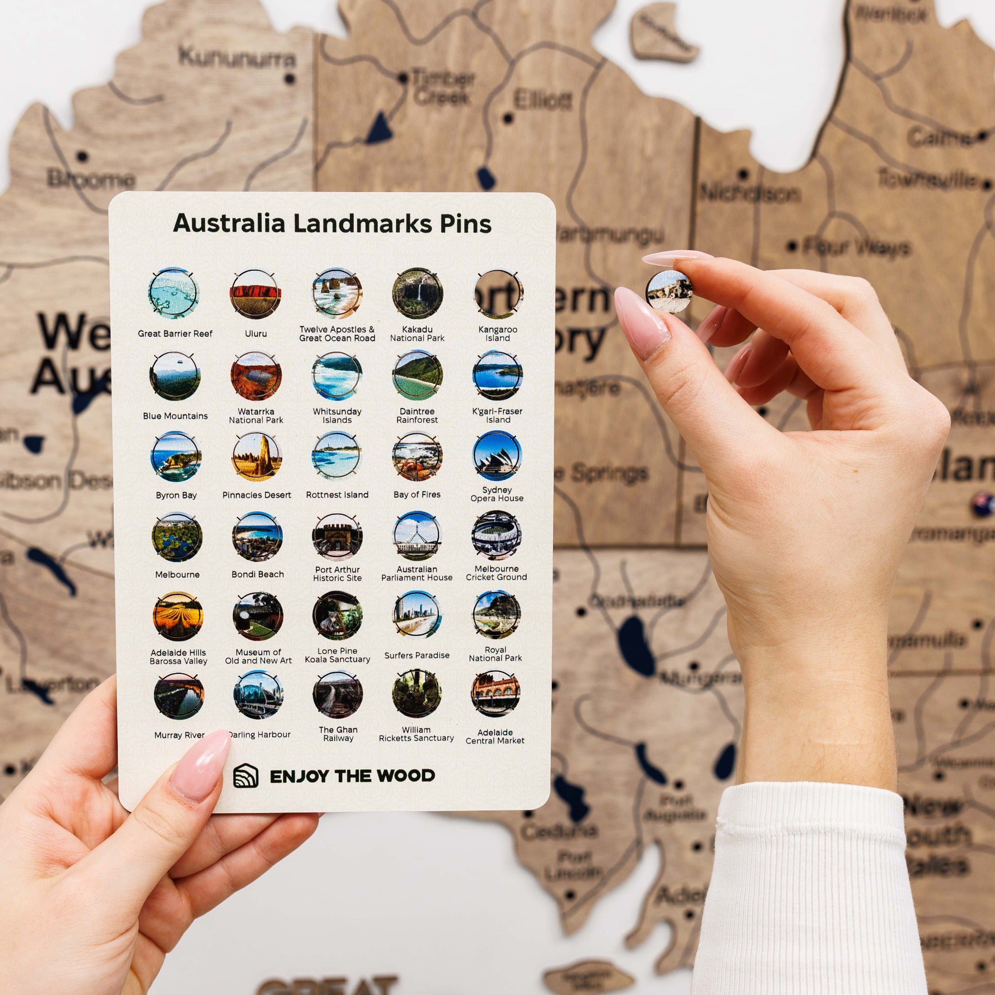 Hand holding a card with Australia landmarks pins against a map background