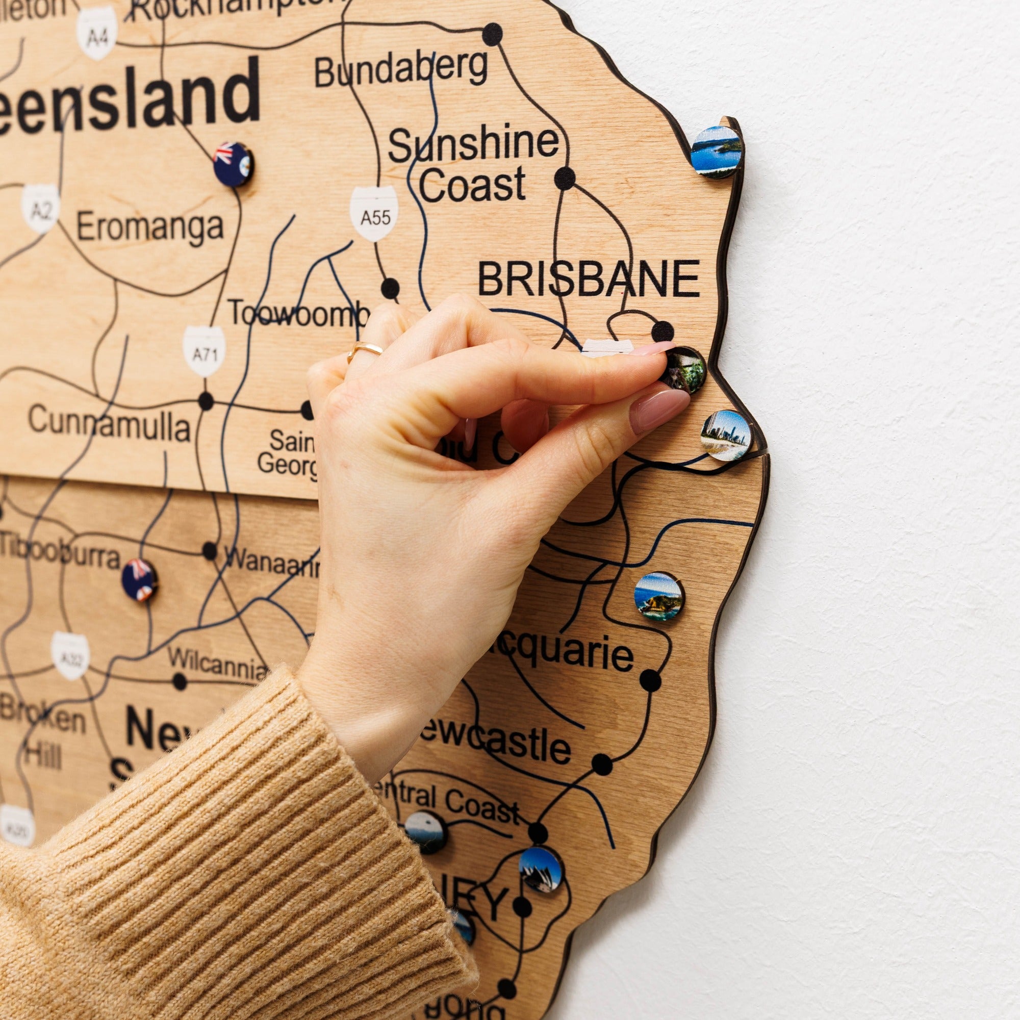Hand placing a wooden pin on a map of Queensland, Australia.