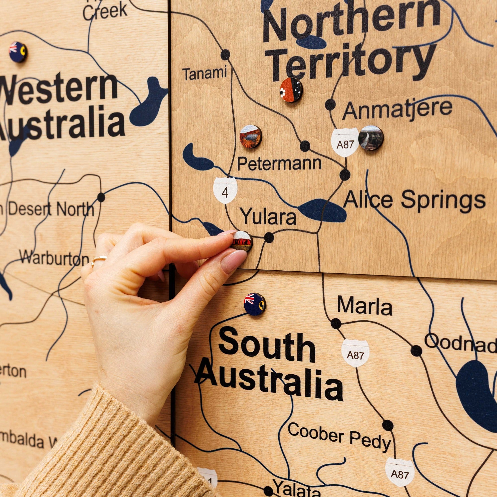 Hand pointing to a map of Australia on a wooden board with pins marking locations.