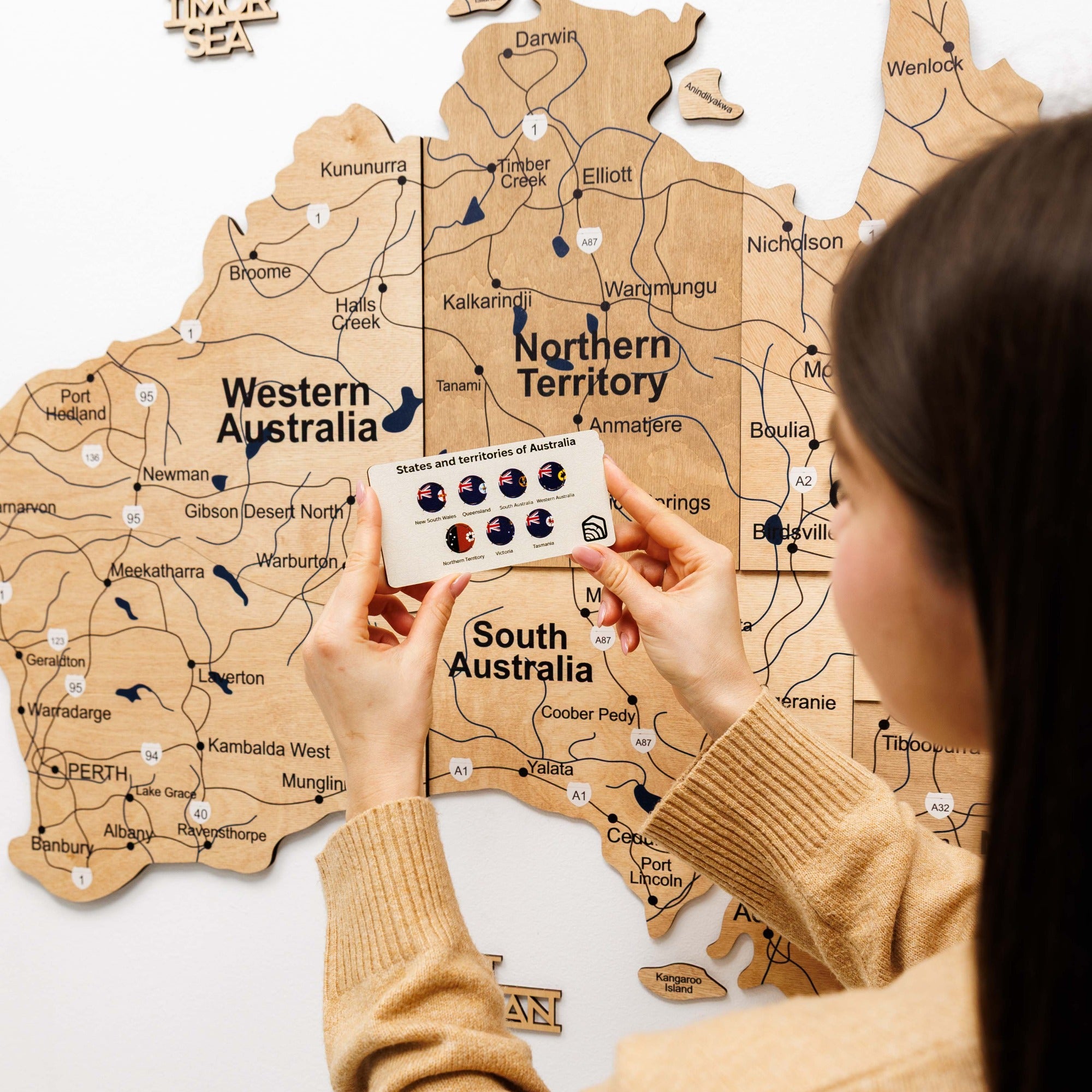 Person holding a card with icons over a wooden map of Australia