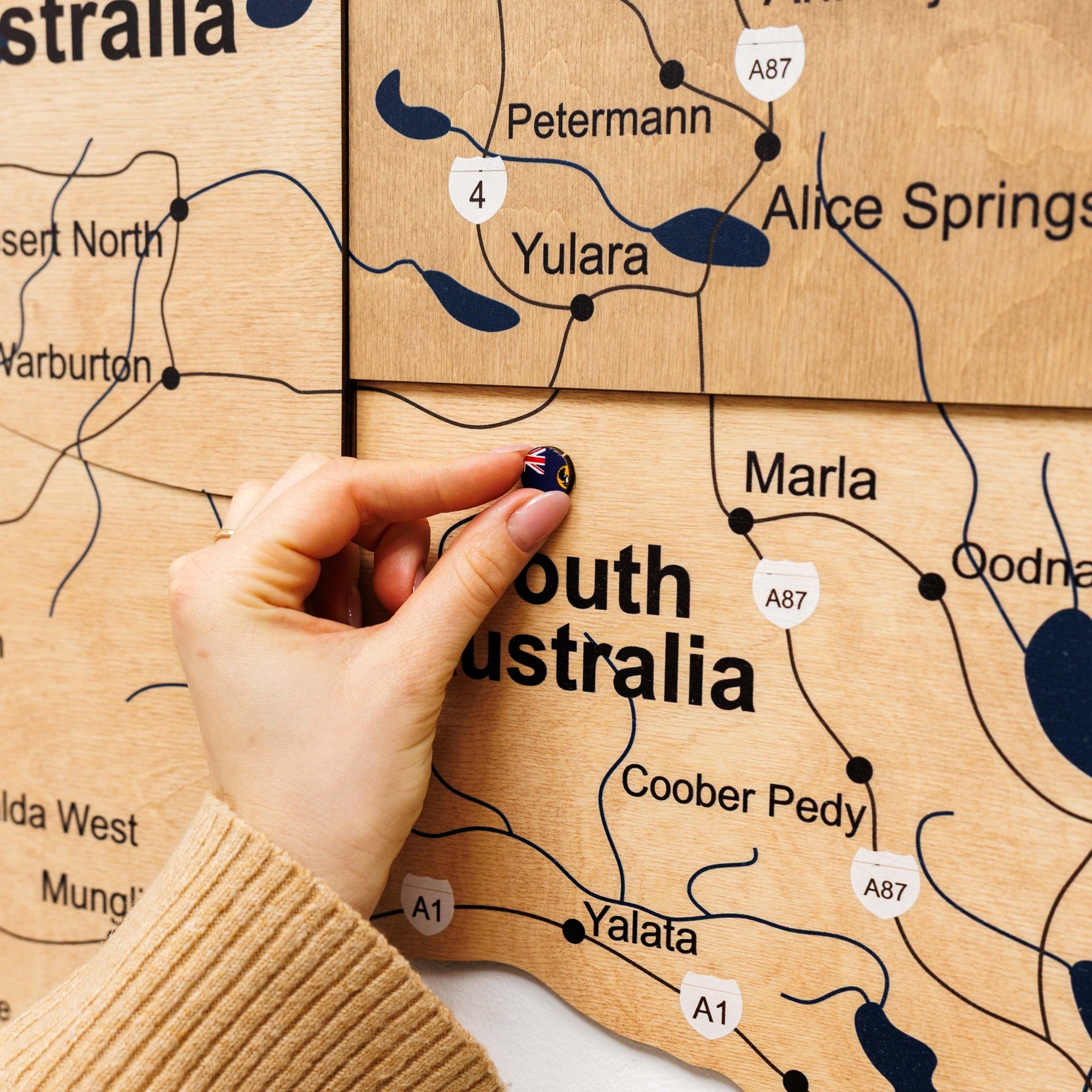 Hand placing a small flag on a wooden map of South Australia