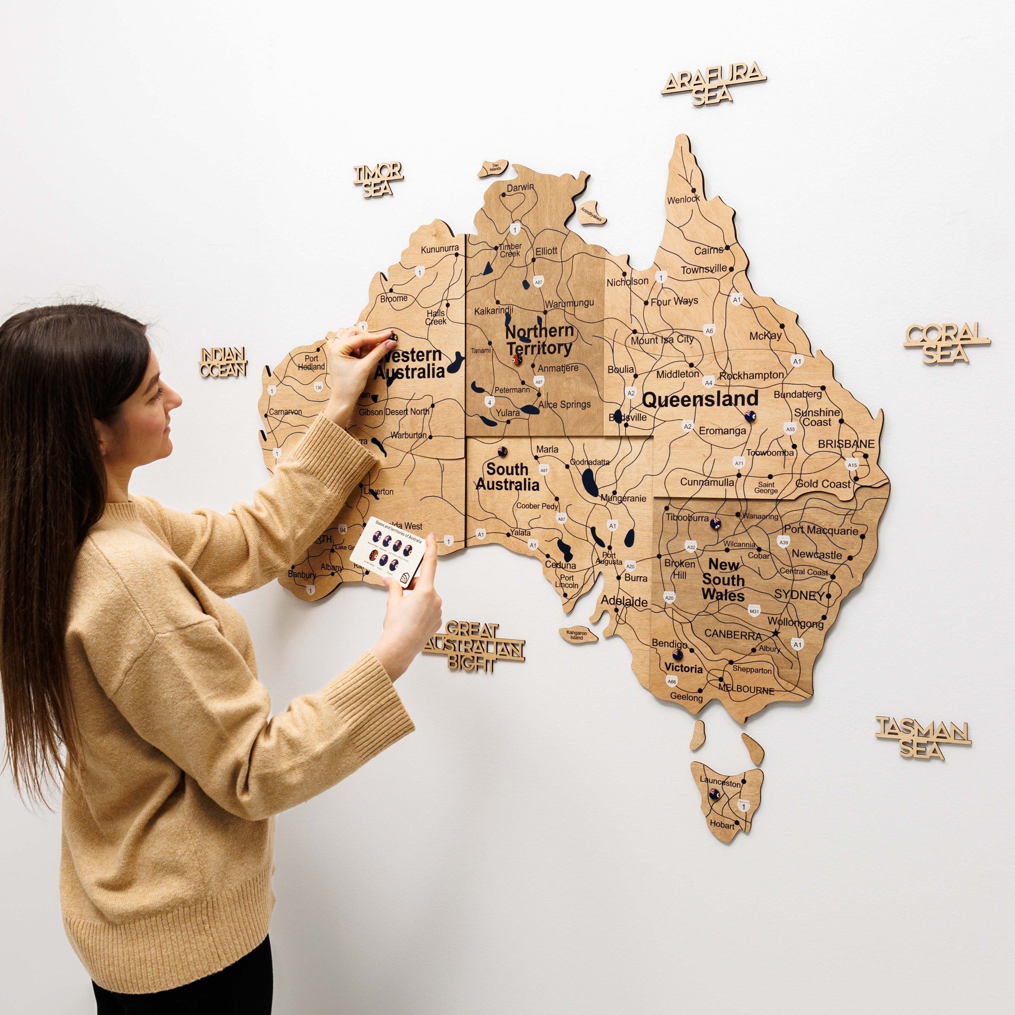Woman interacting with a wooden map of Australia on a white wall