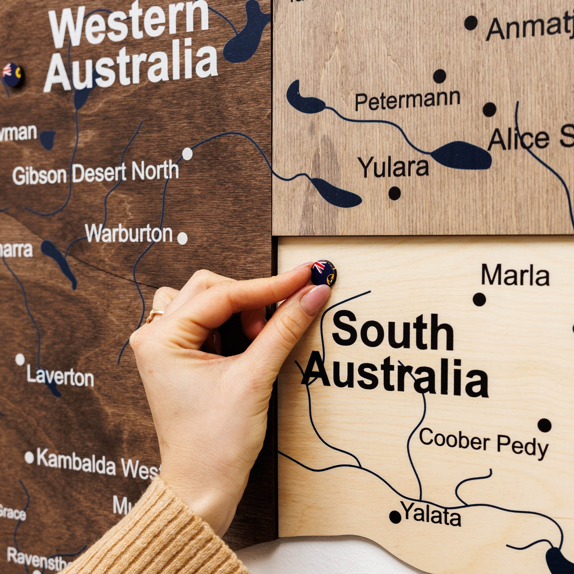 Hand placing a small flag on a wooden map of Australia, highlighting Western Australia and South Australia.
