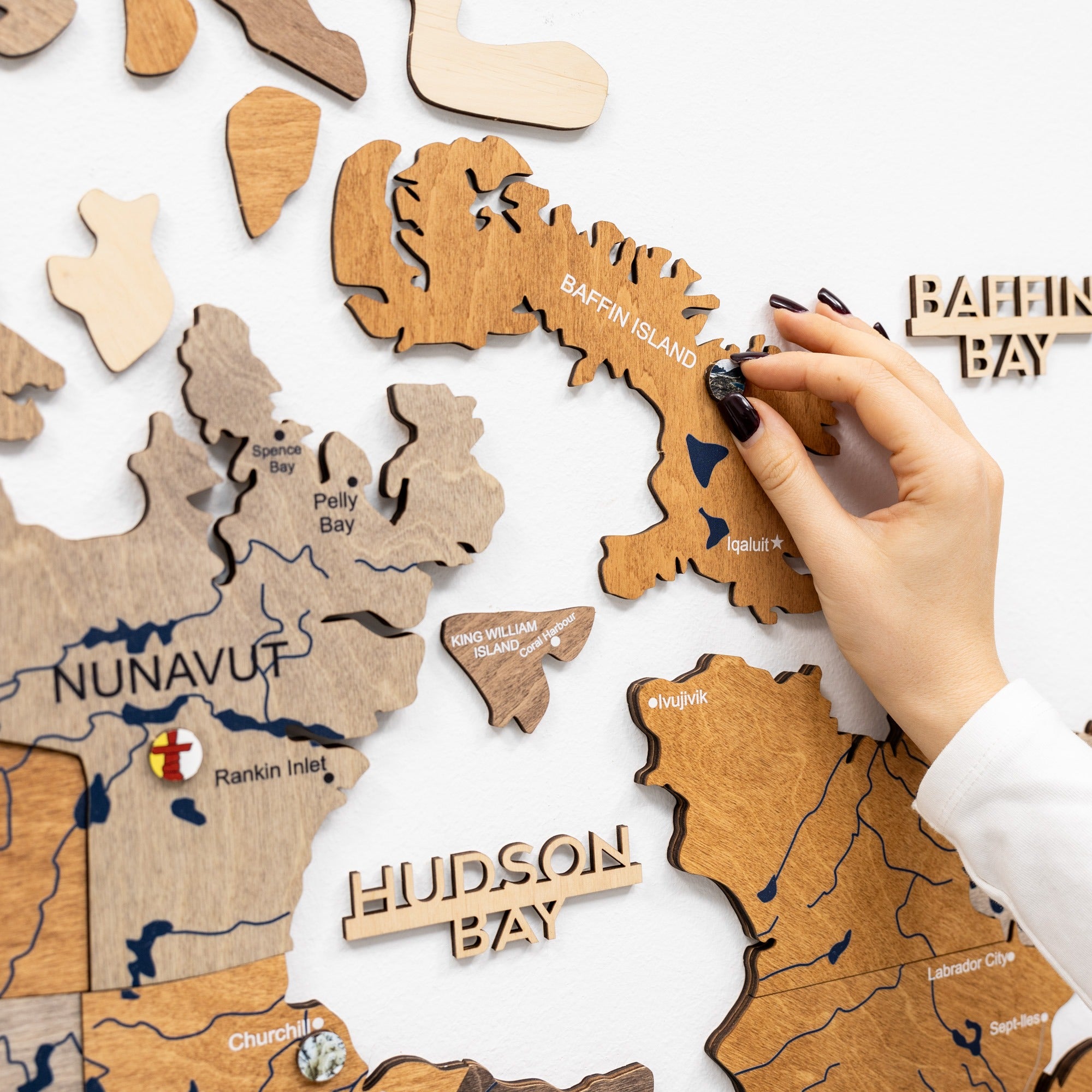 Wooden puzzle map of Canada with a hand placing a piece labeled 'Baffin Island'.