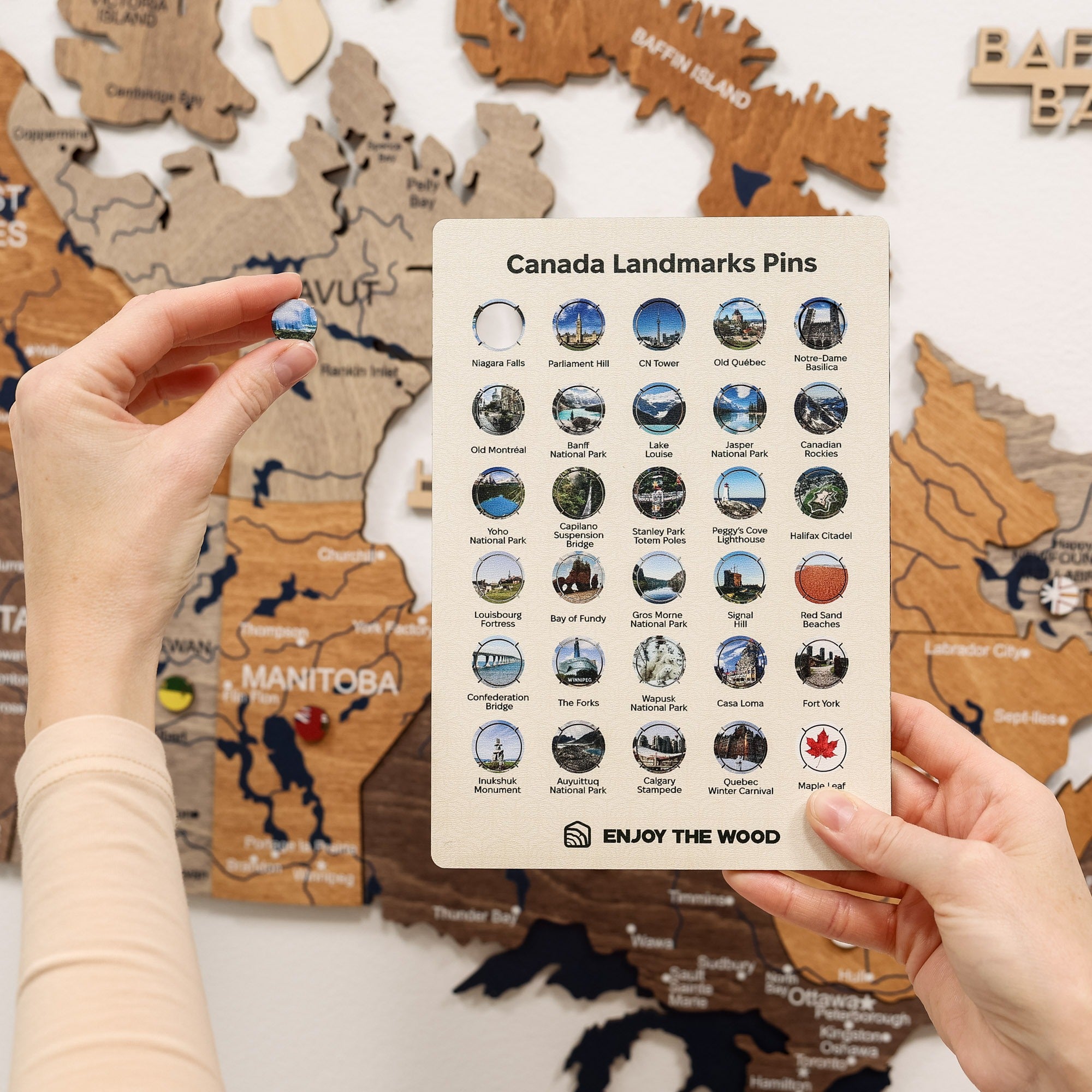 Hand holding a card with Canada landmarks pins in front of a wooden map of Canada.