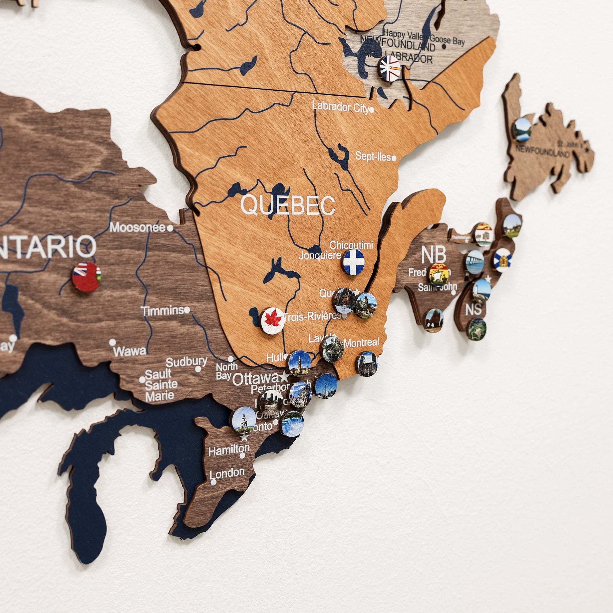 Wooden map of Canada with various locations marked by pins on a white background