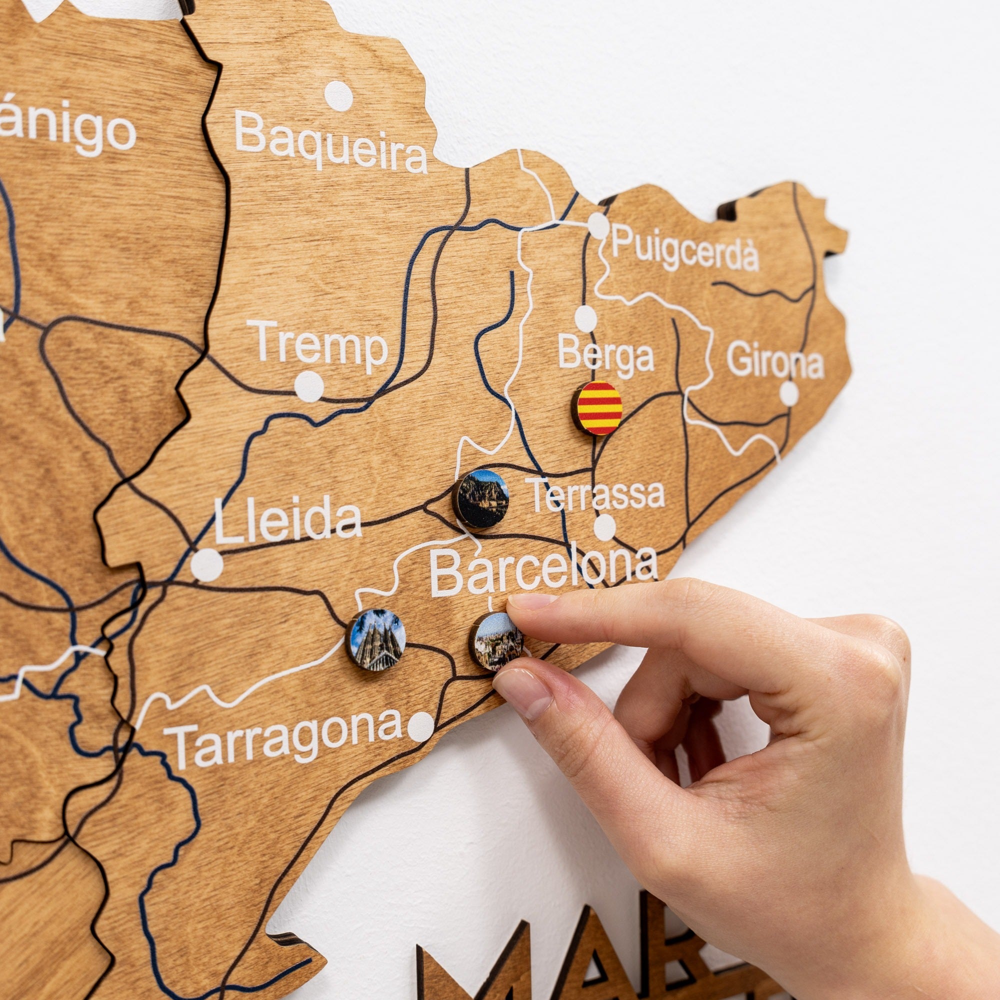 Hand placing a pin on a wooden map of Catalonia, Spain.