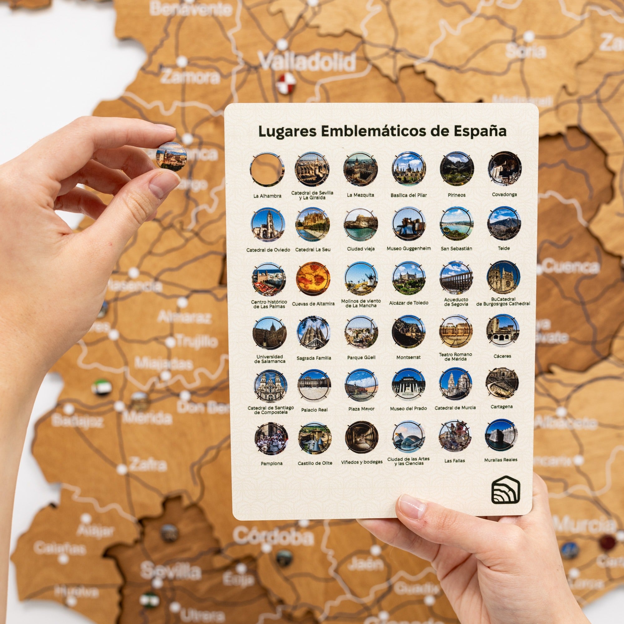 Hand holding a card with emblematic places of Spain against a map background