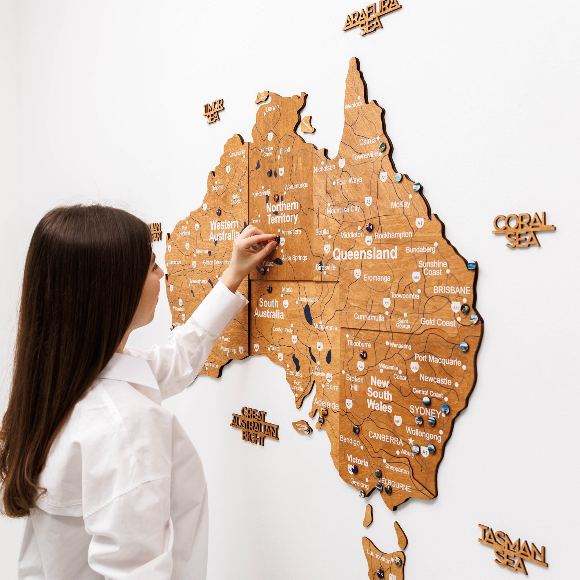 Woman interacting with a wooden map of Australia on a white wall