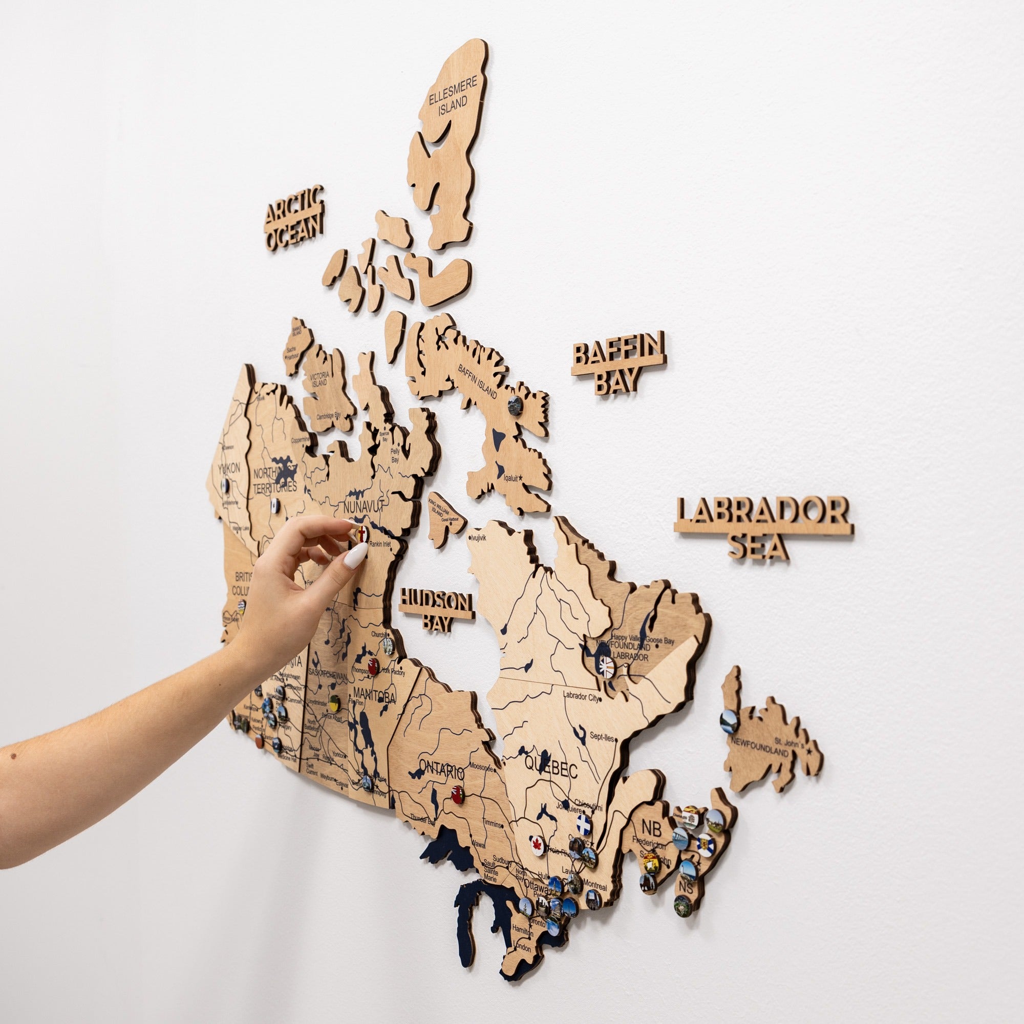 Wooden map of Canada with a hand pointing to a location on the map.
