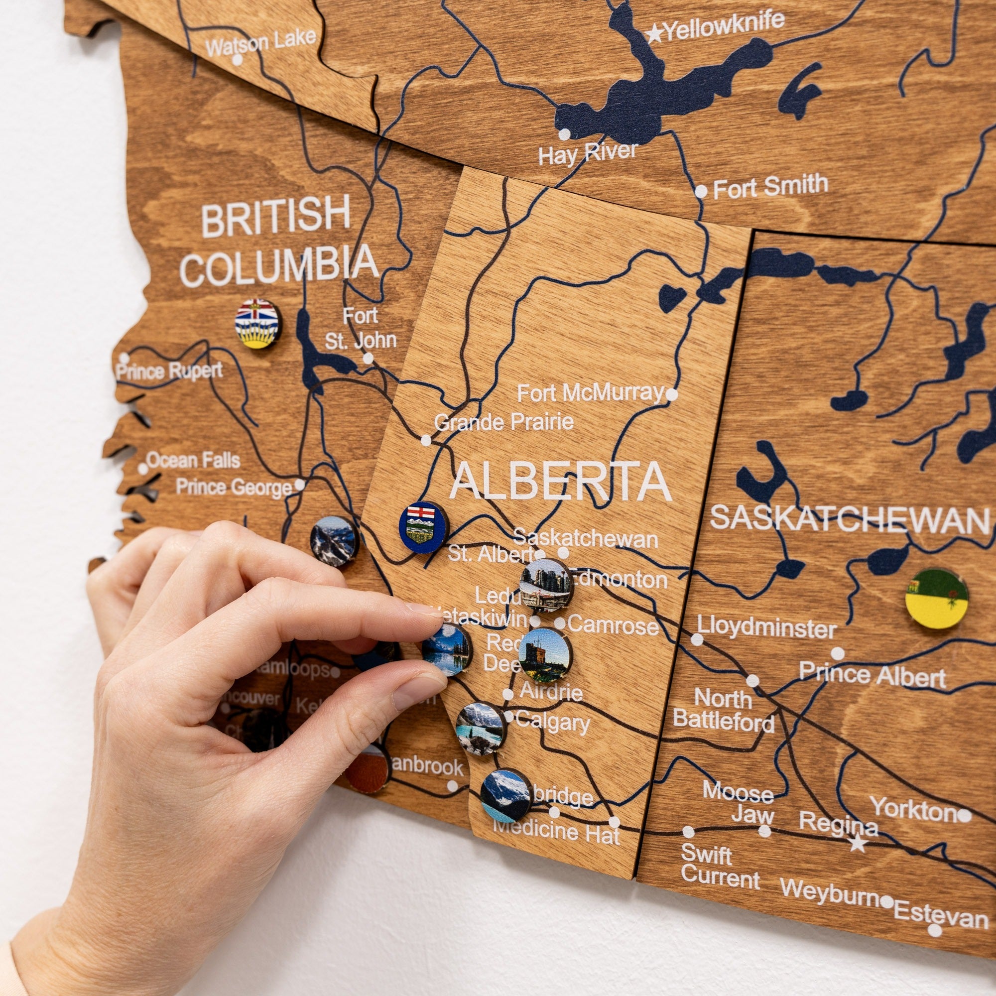 Wooden map of Canada with pins marking locations, held by a hand.