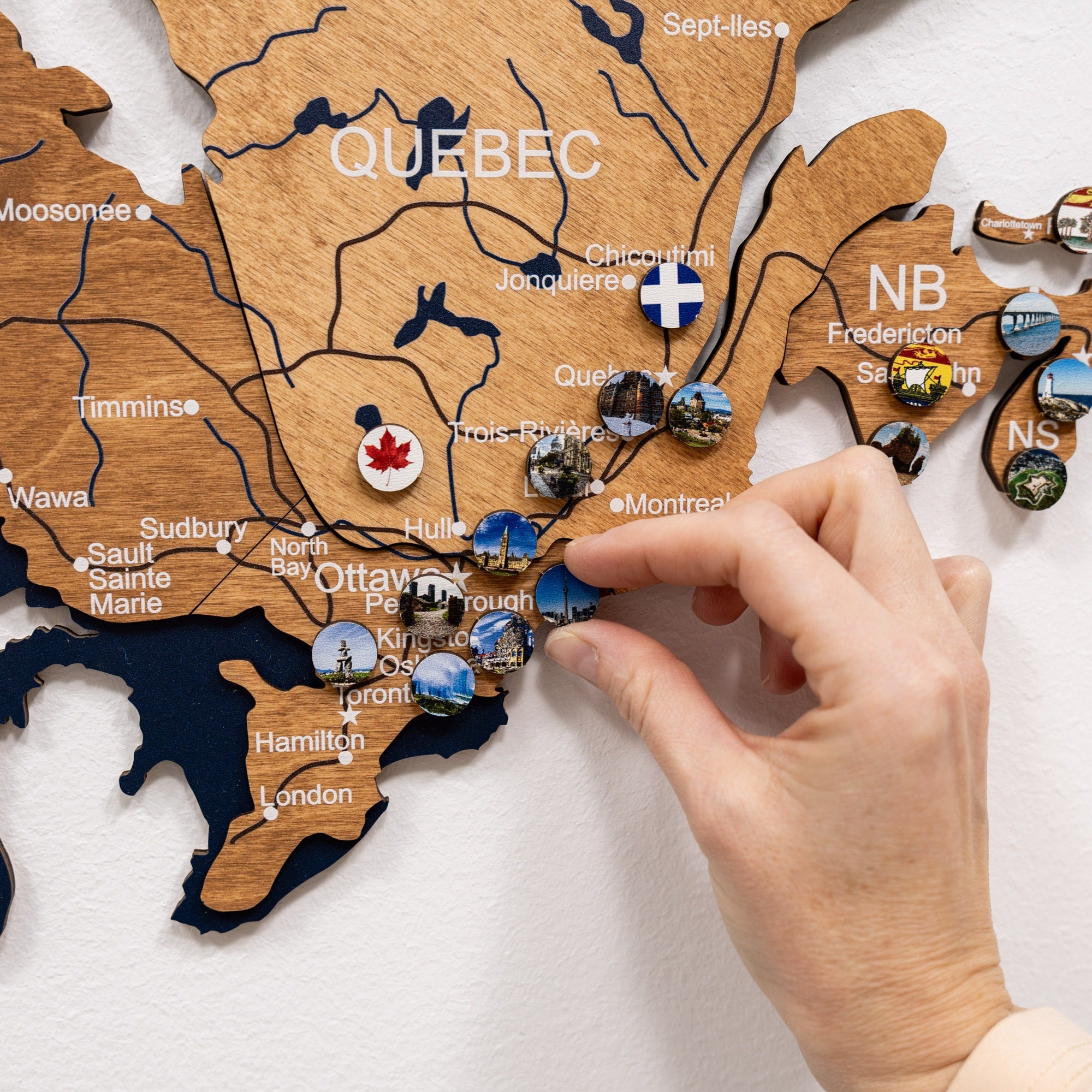 Wooden map of Canada with pins marking locations, including a hand interacting with it.
