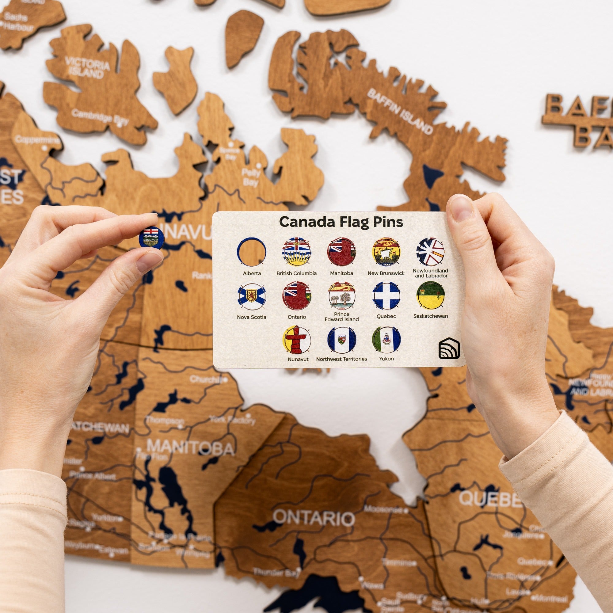 Wooden map of Canada with hands holding a card with flag pins in front