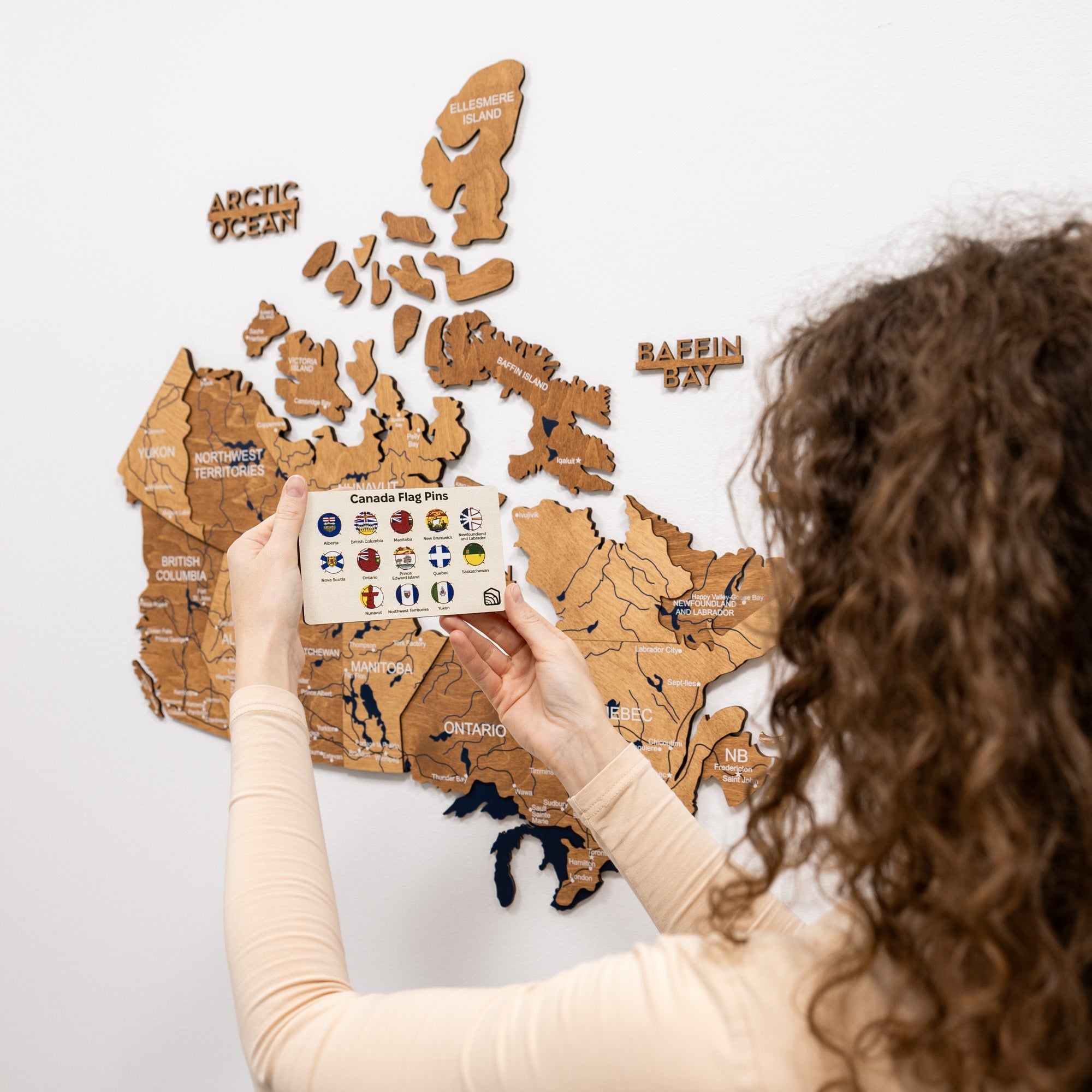 Person holding a card with flag pins over a wooden map of Canada.