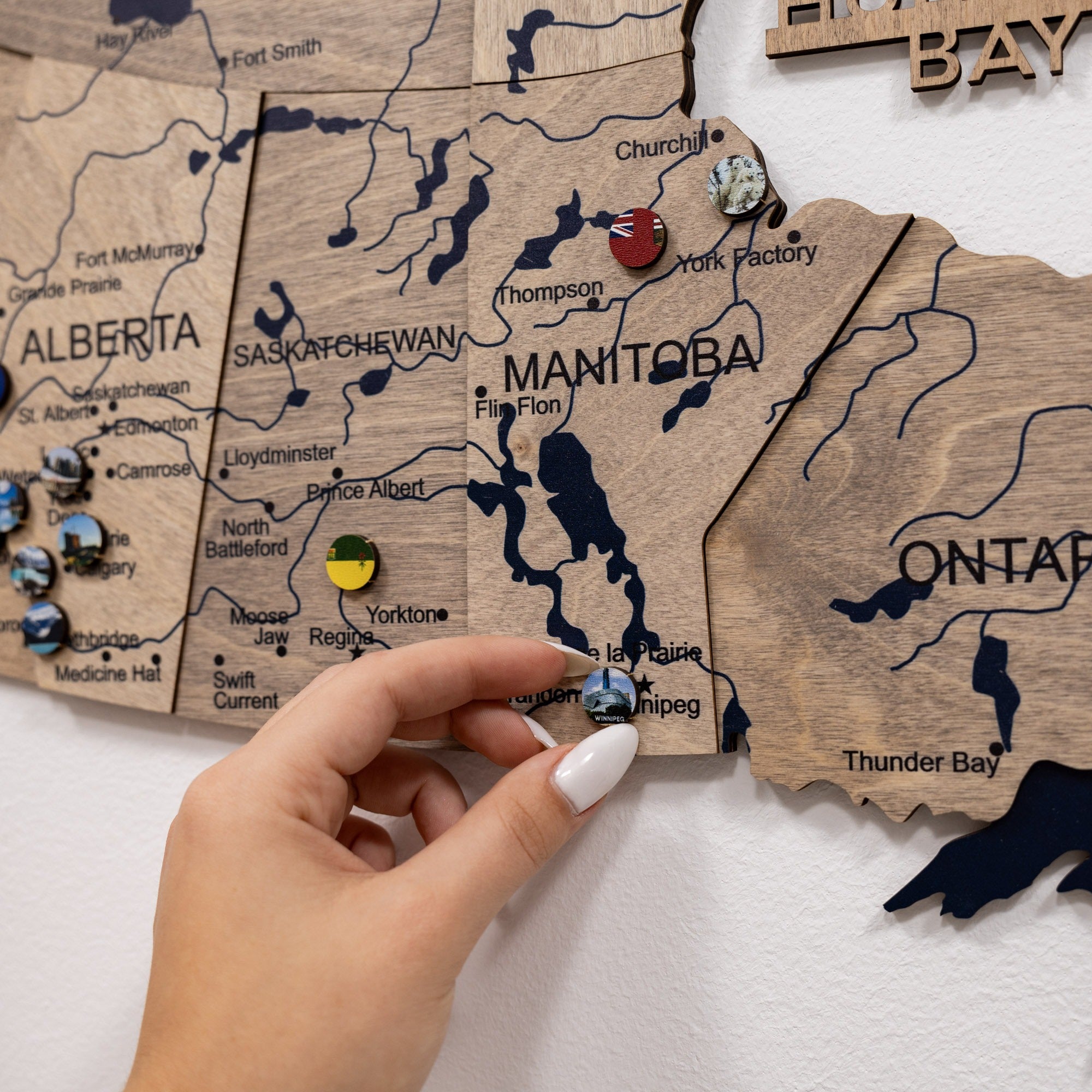 Wooden map of Canada with pins marking locations, held by a hand.
