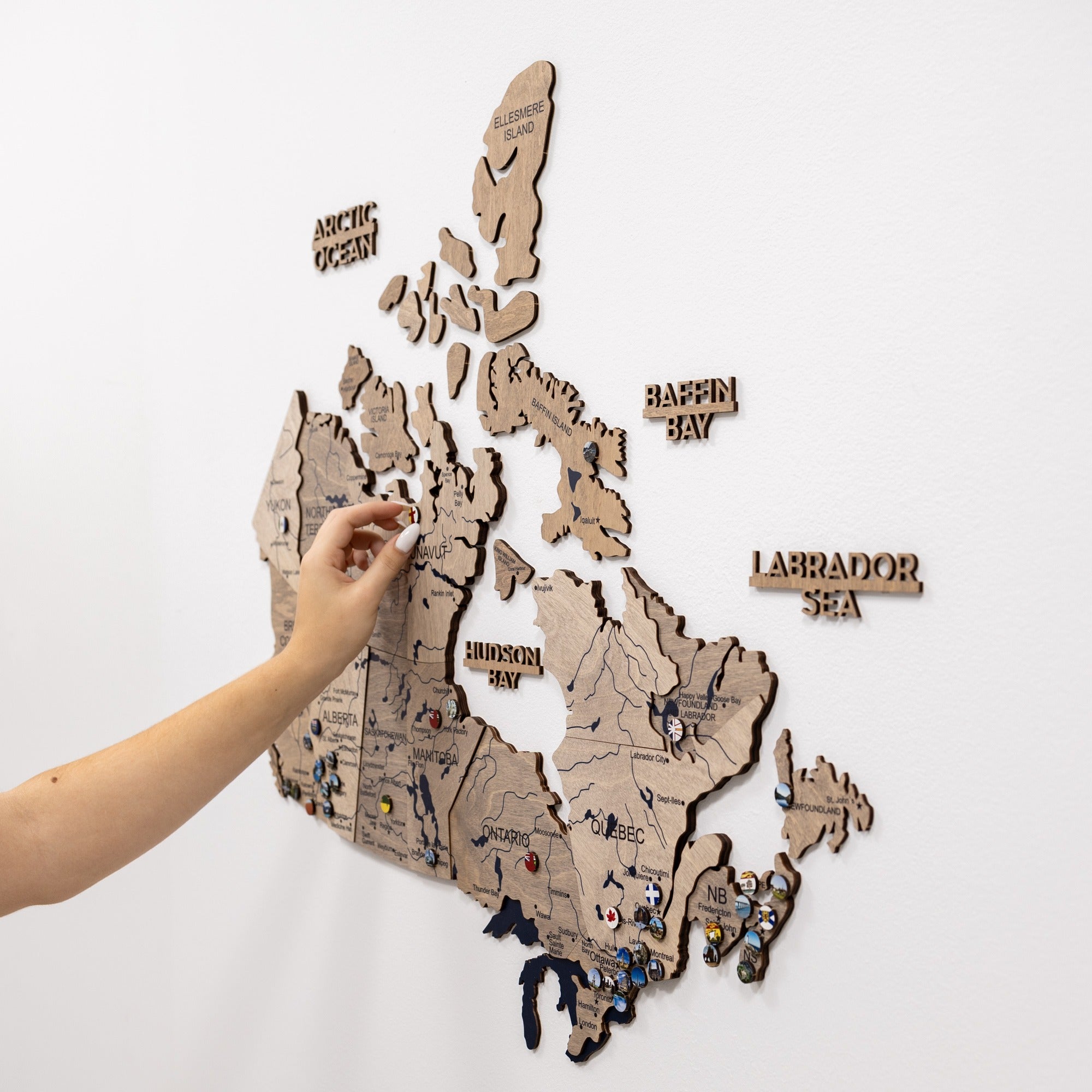 Wooden map of Canada with pins on a white background