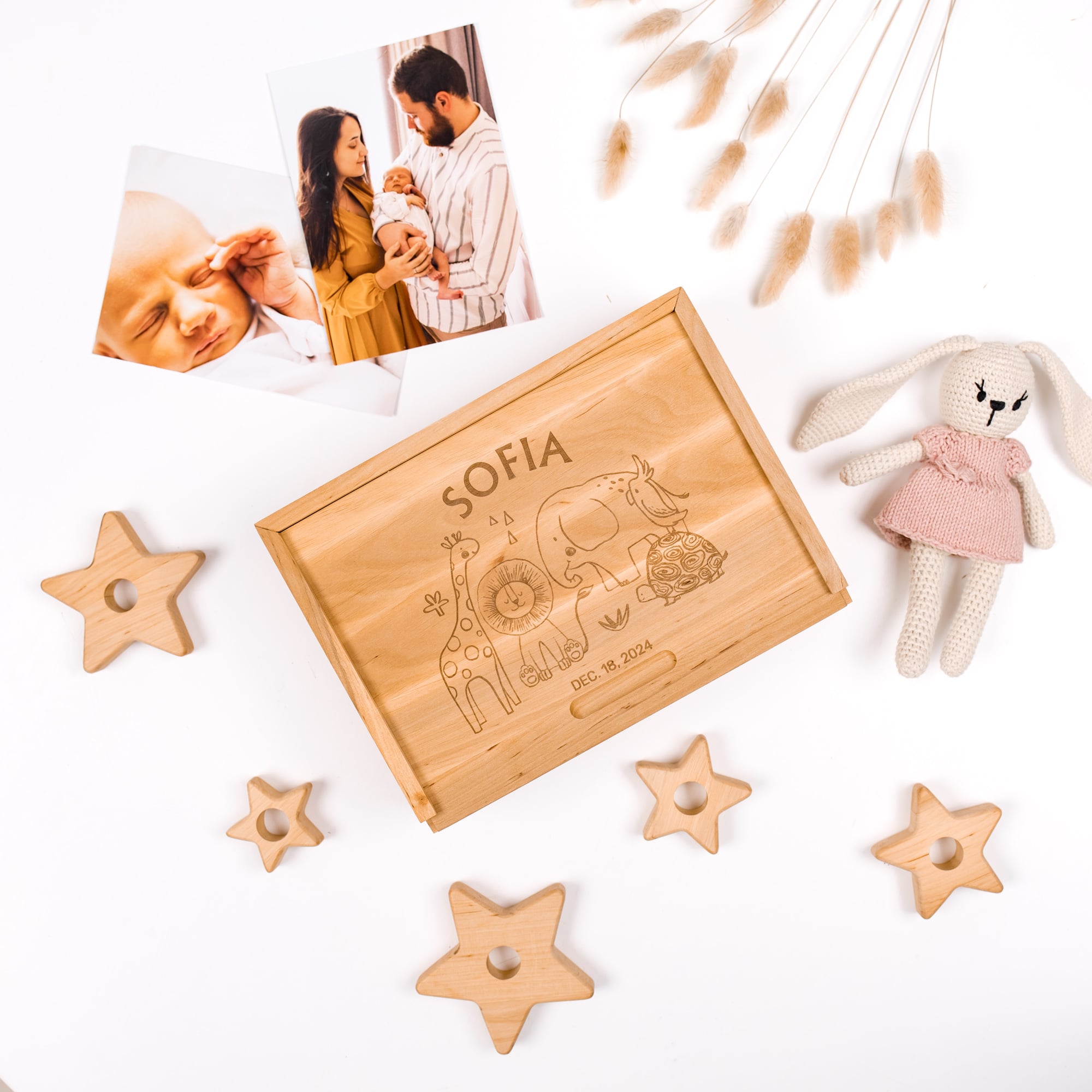 Wooden box with engraved design and text, surrounded by star-shaped wooden toys and a plush rabbit toy on a white background.