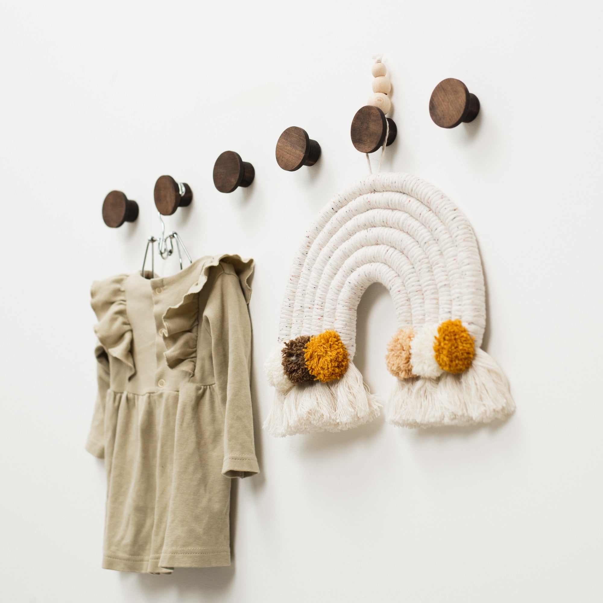 Wall hooks with a dress and decorative rainbow on a white wall