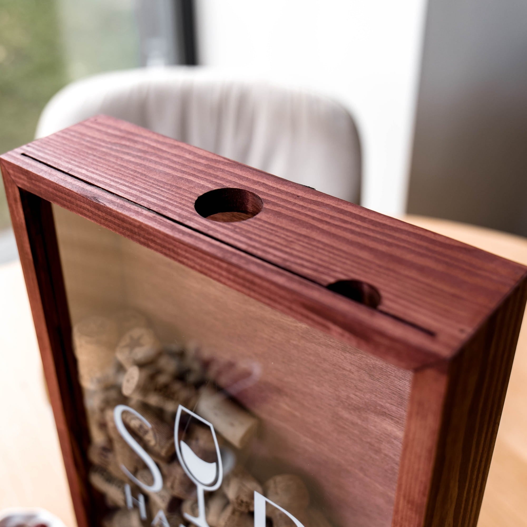 The box has a reddish-brown wood grain finish and a circular hole on top, with a white logo partially visible on the glass.