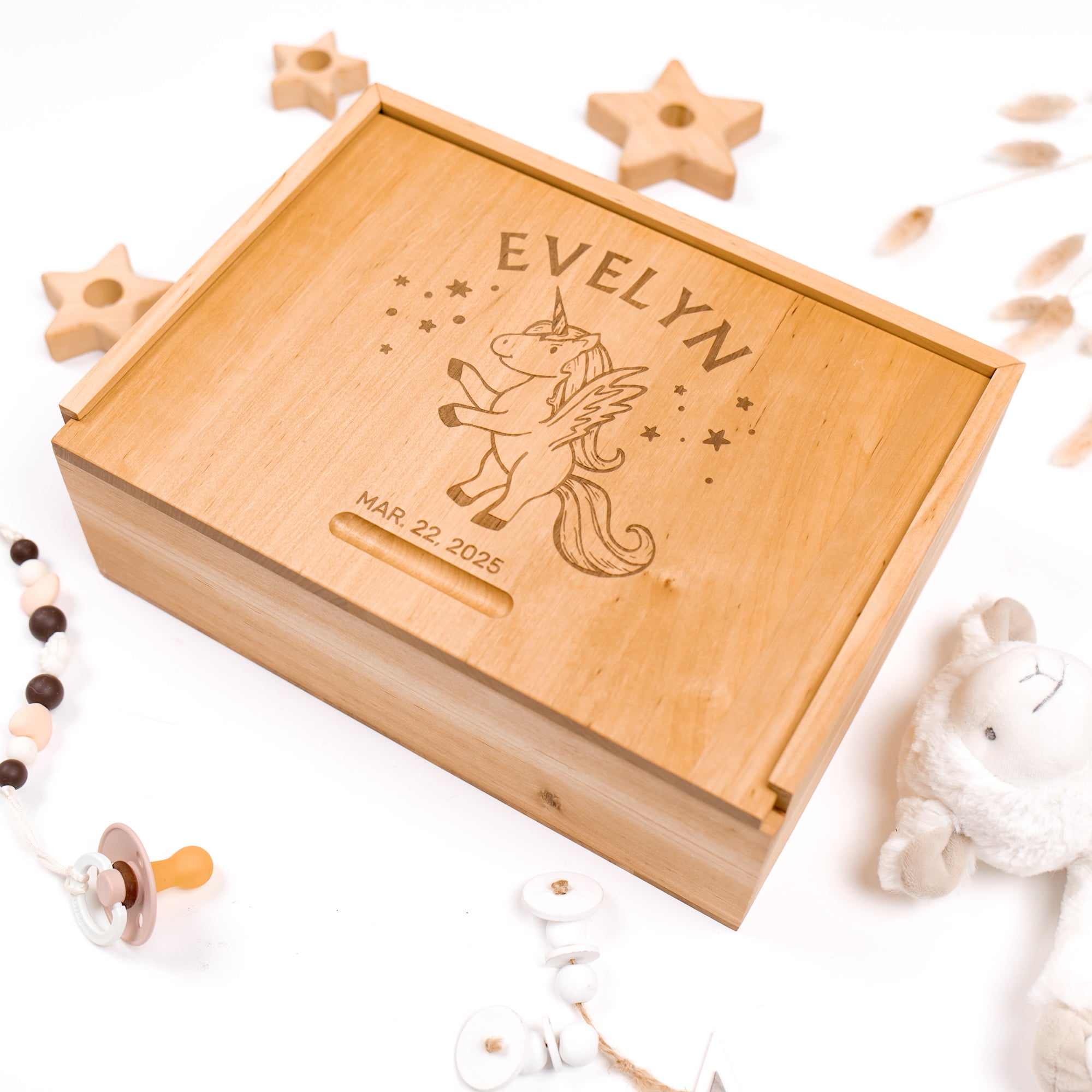 Wooden box engraved with 'EVELYN' and a unicorn design, surrounded by baby toys on a white background.