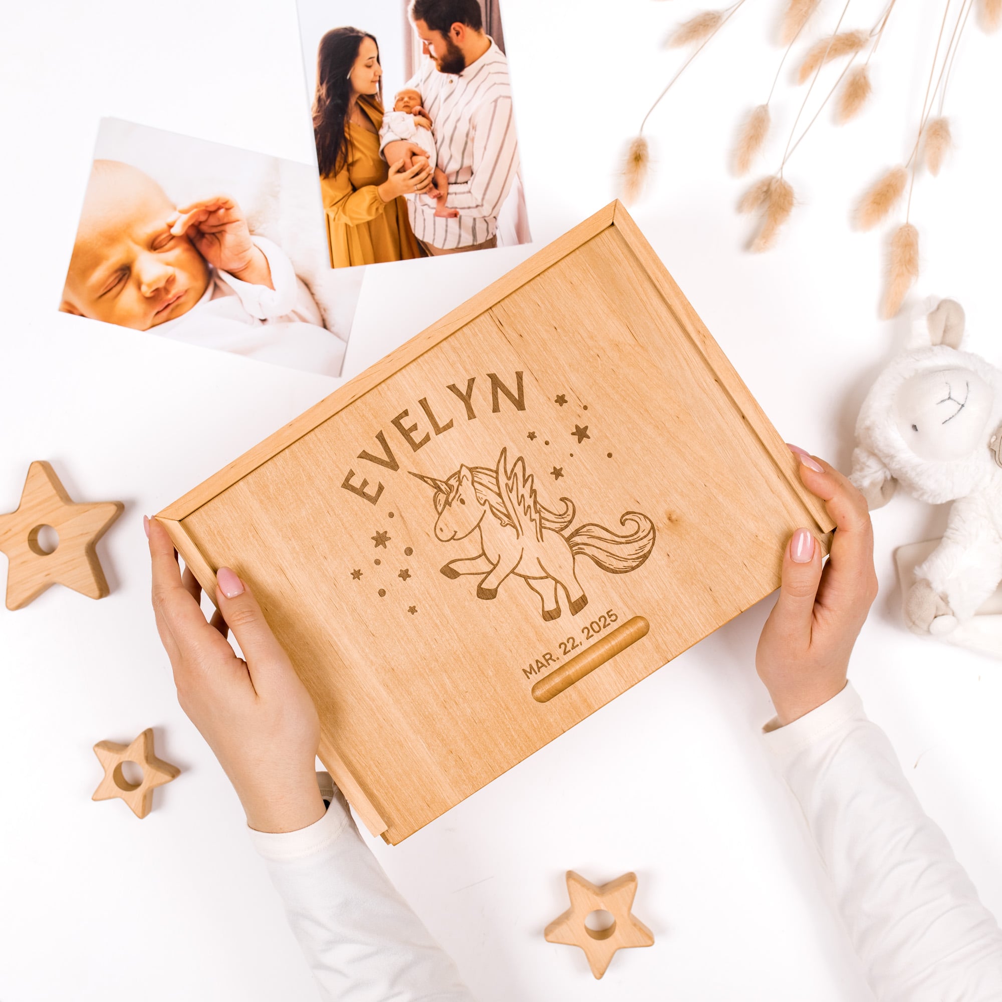 Wooden box with engraved name and unicorn design, held by hands on a white surface with photos and decor.