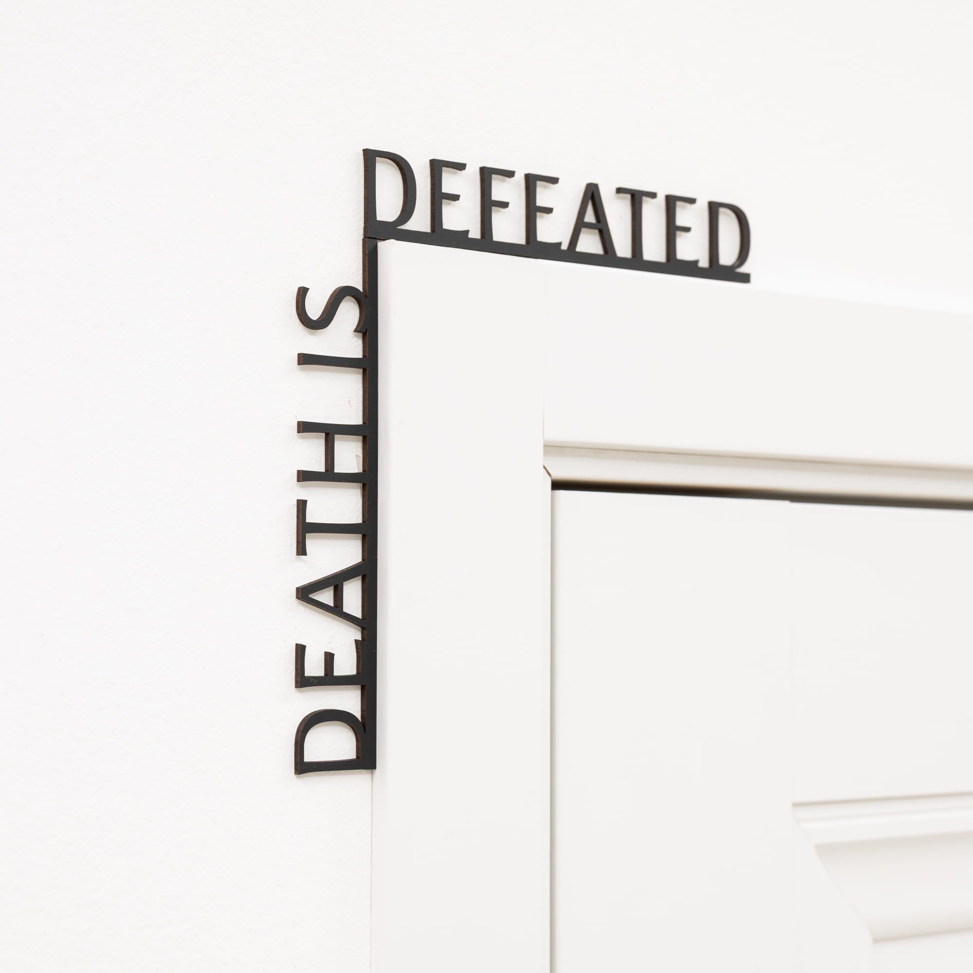 Decorative wall art with 'DEFEATED' and 'DEATH IS' text on a white background