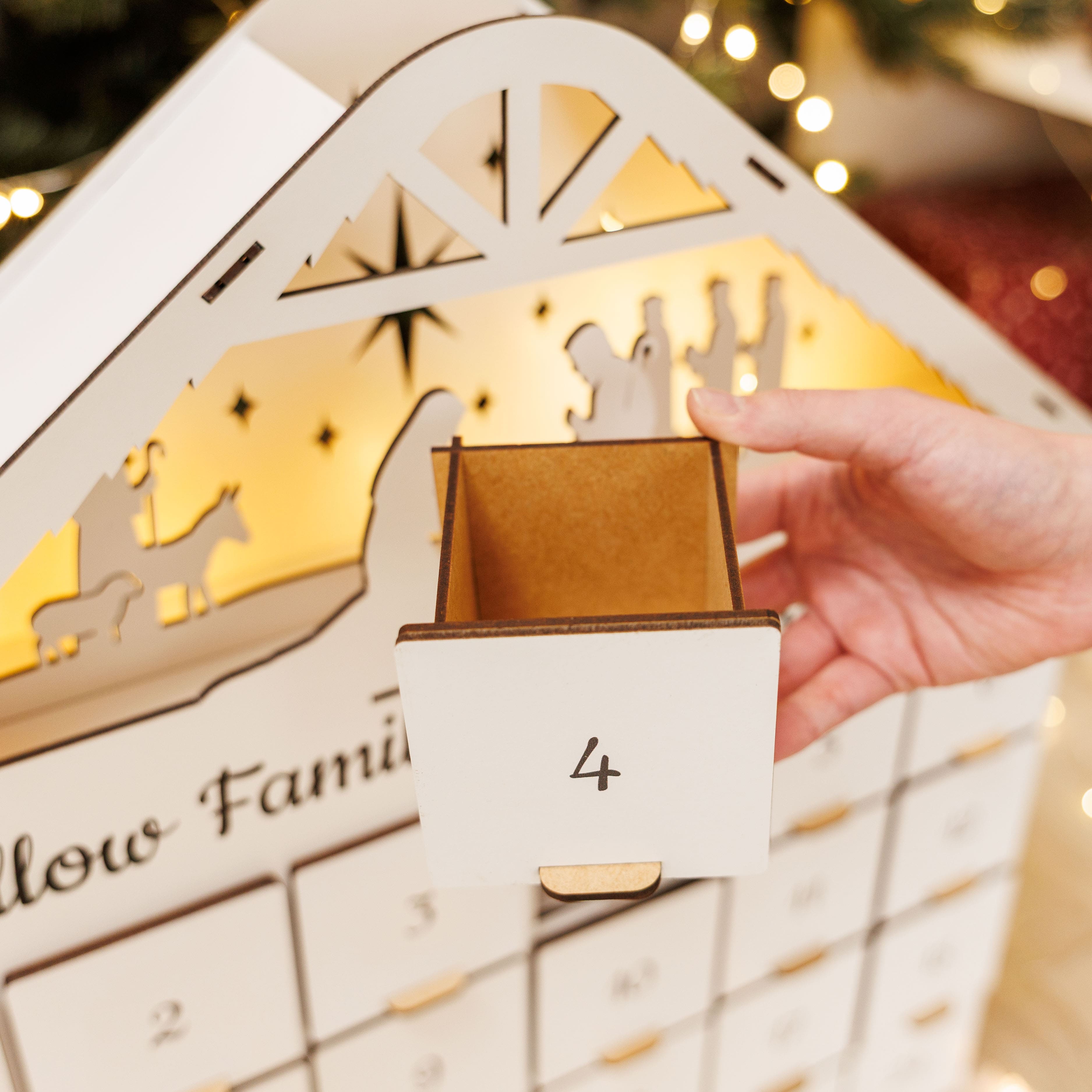 Advent calendar with a hand pulling out a door, Christmas lights in the background