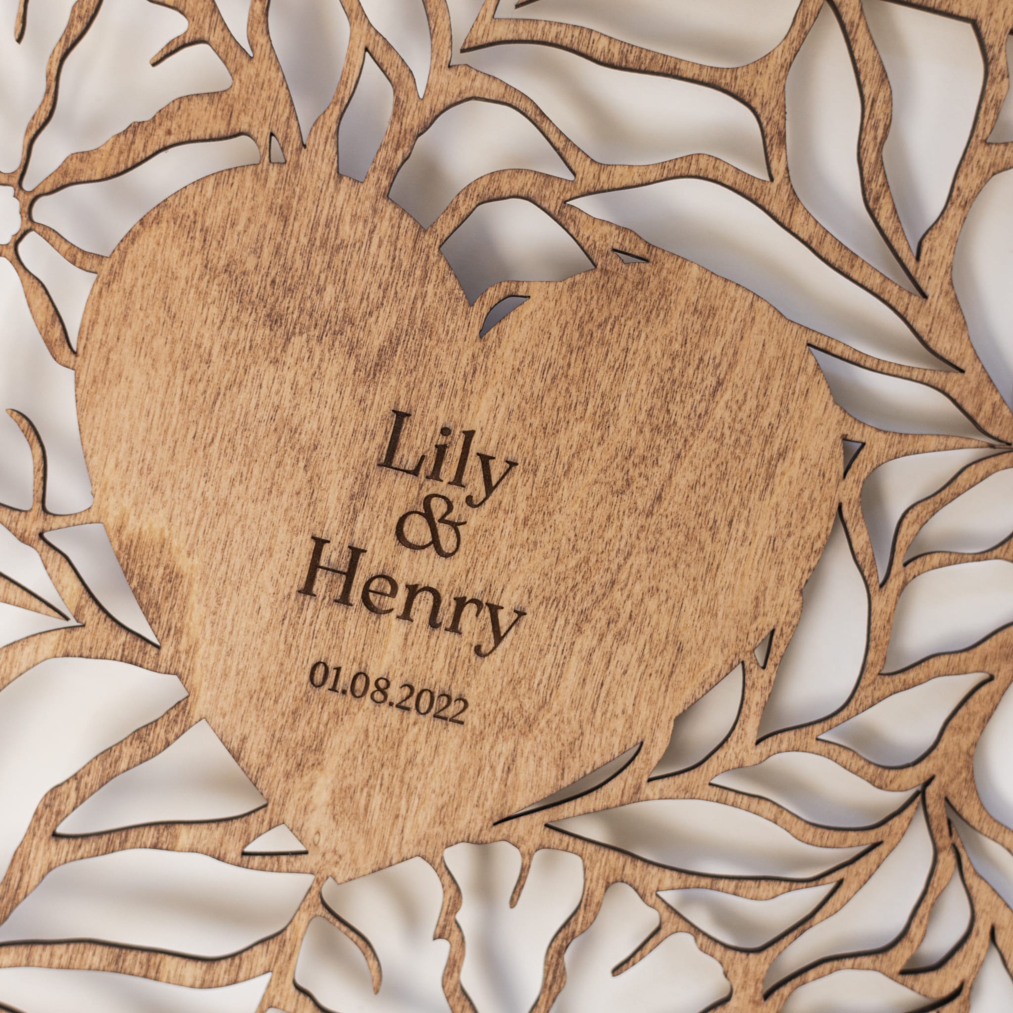 Wooden heart-shaped plaque with engraved names and date, surrounded by leaf patterns.
