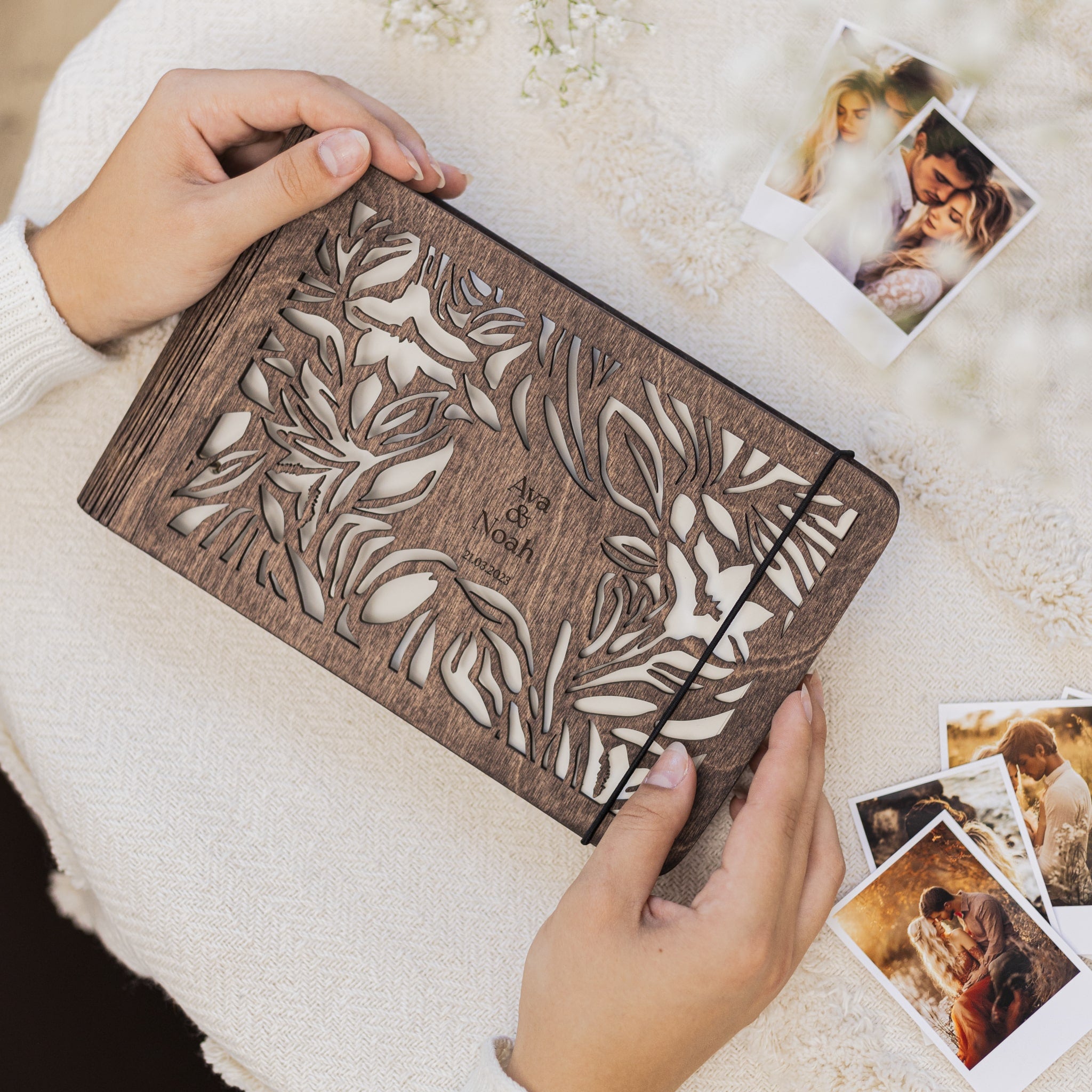 Wooden photo album with floral design held by hands on a light background with photos.