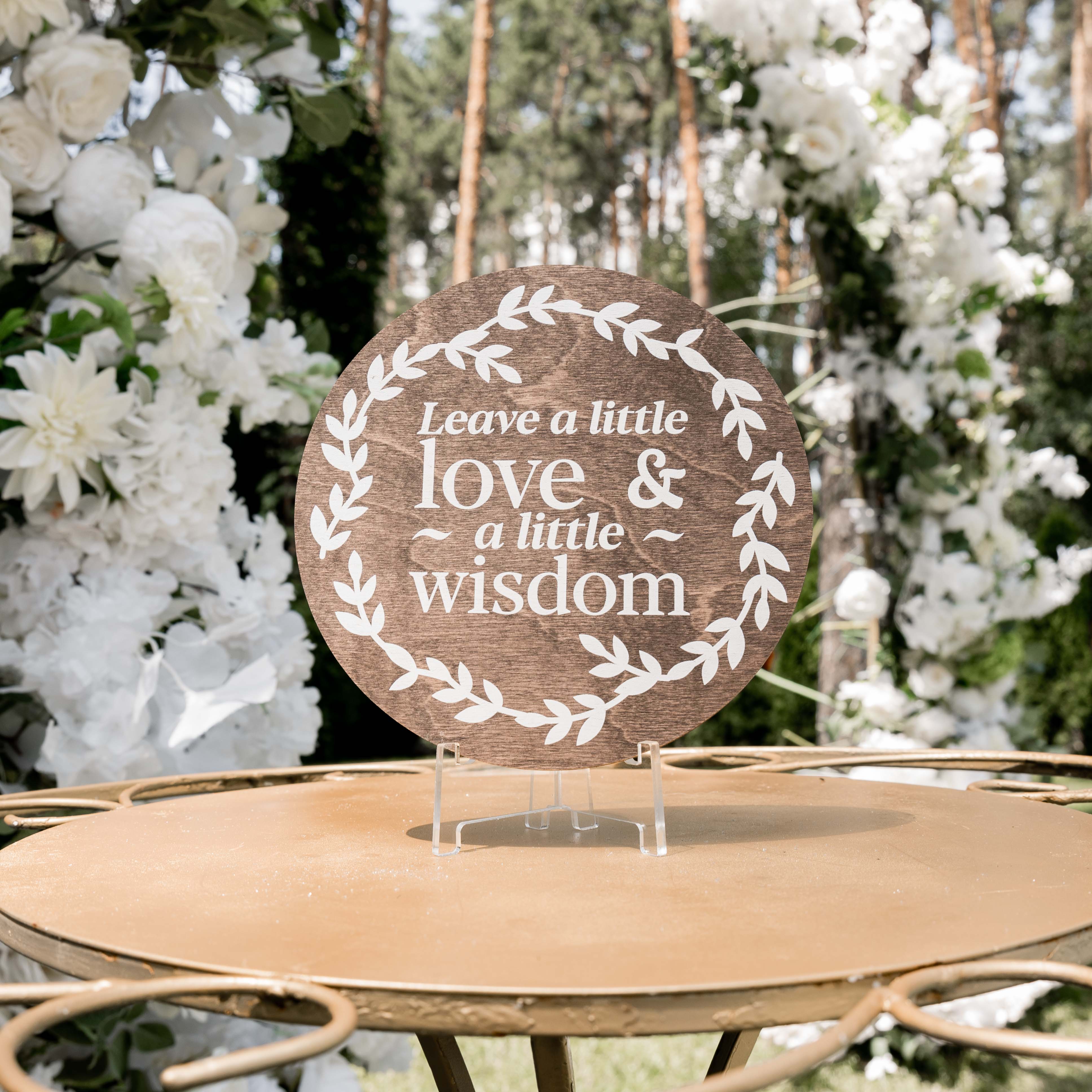 Decorative sign with 'Leave a little love & a little wisdom' text on a stand with floral background