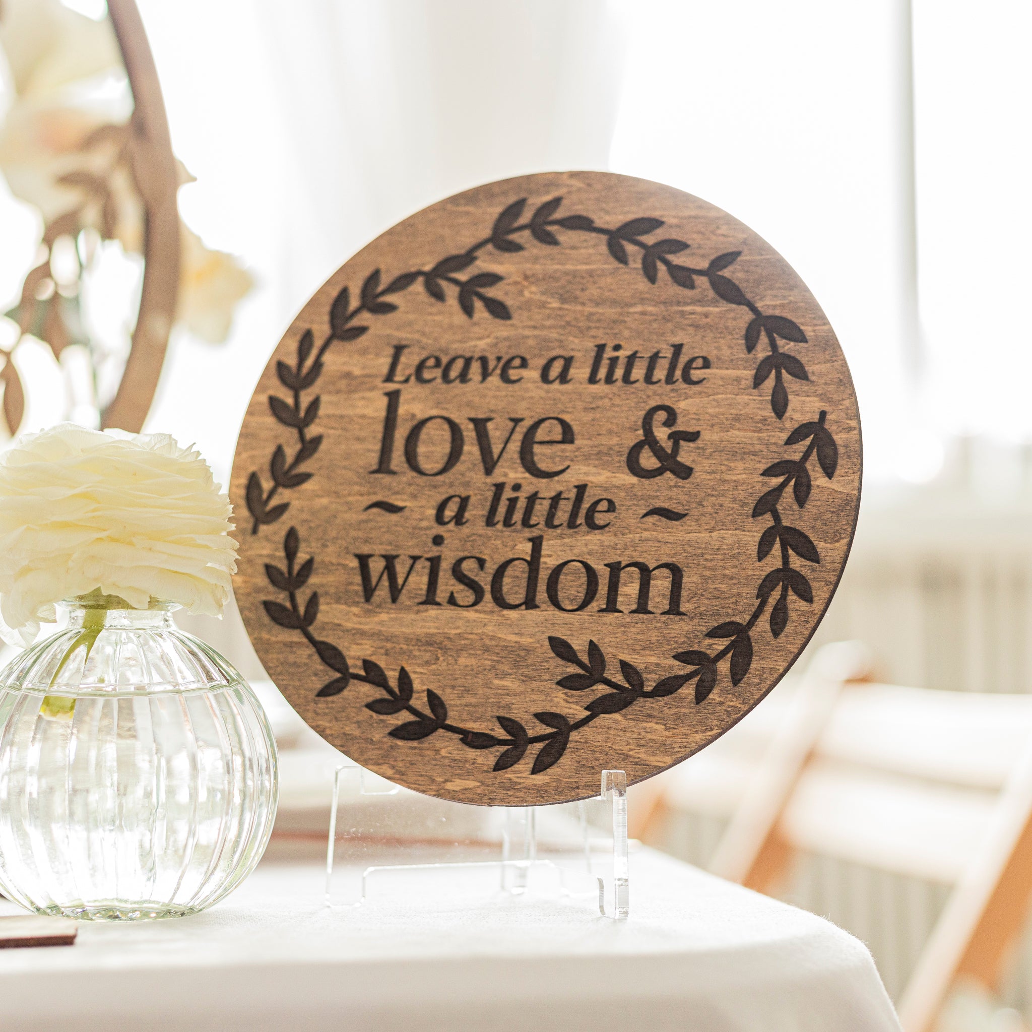 Wooden plaque with engraved text 'Leave a little love & a little wisdom' on a stand.