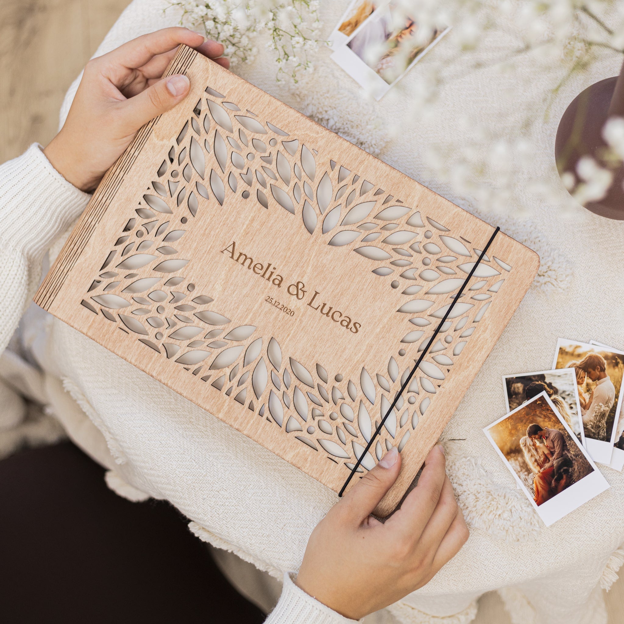Wooden album with laser cut design held by a person, with 'Amelia & Lucas' engraved on it.