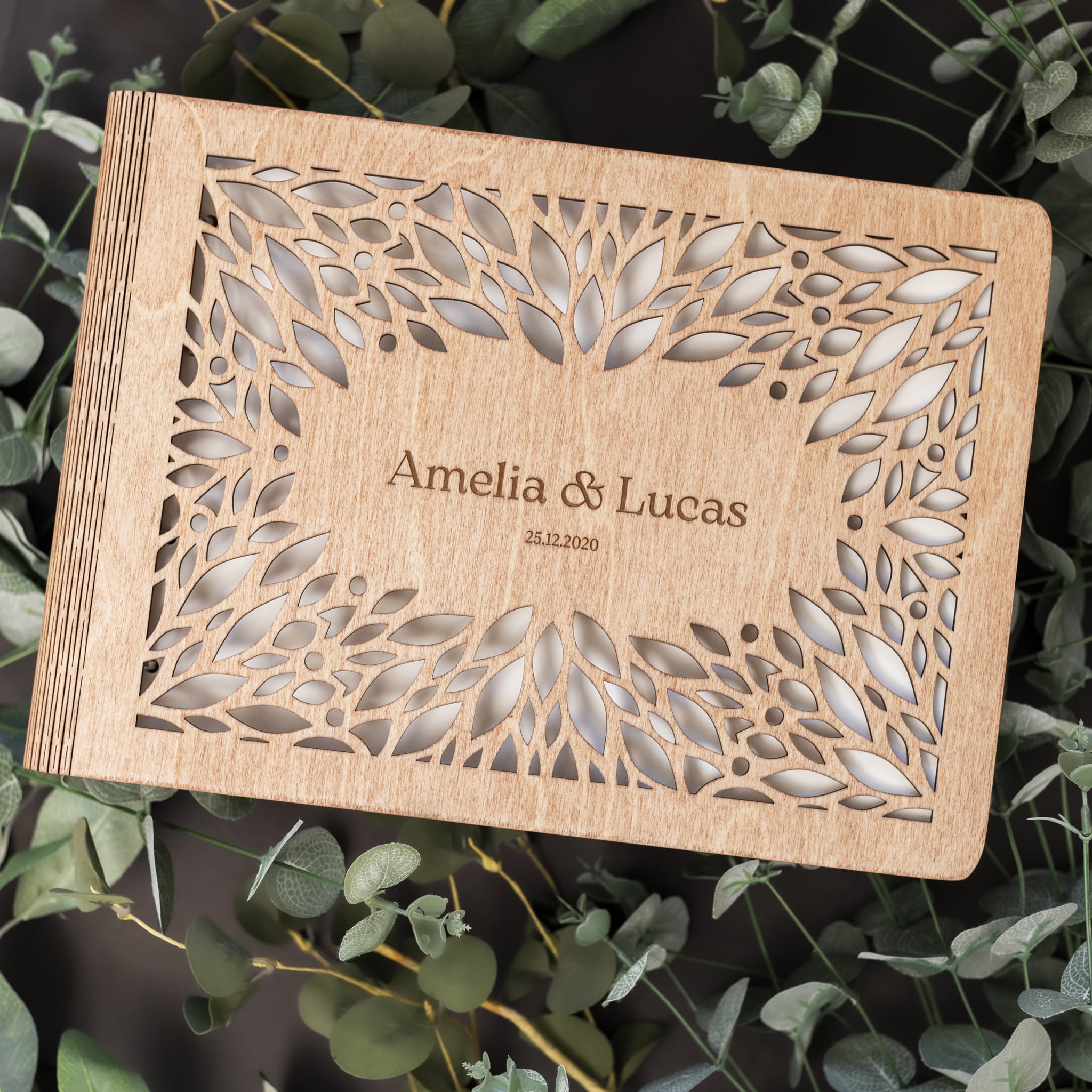 Wooden wedding invitation with laser cut design and 'Amelia & Lucas' text on a green leaf background